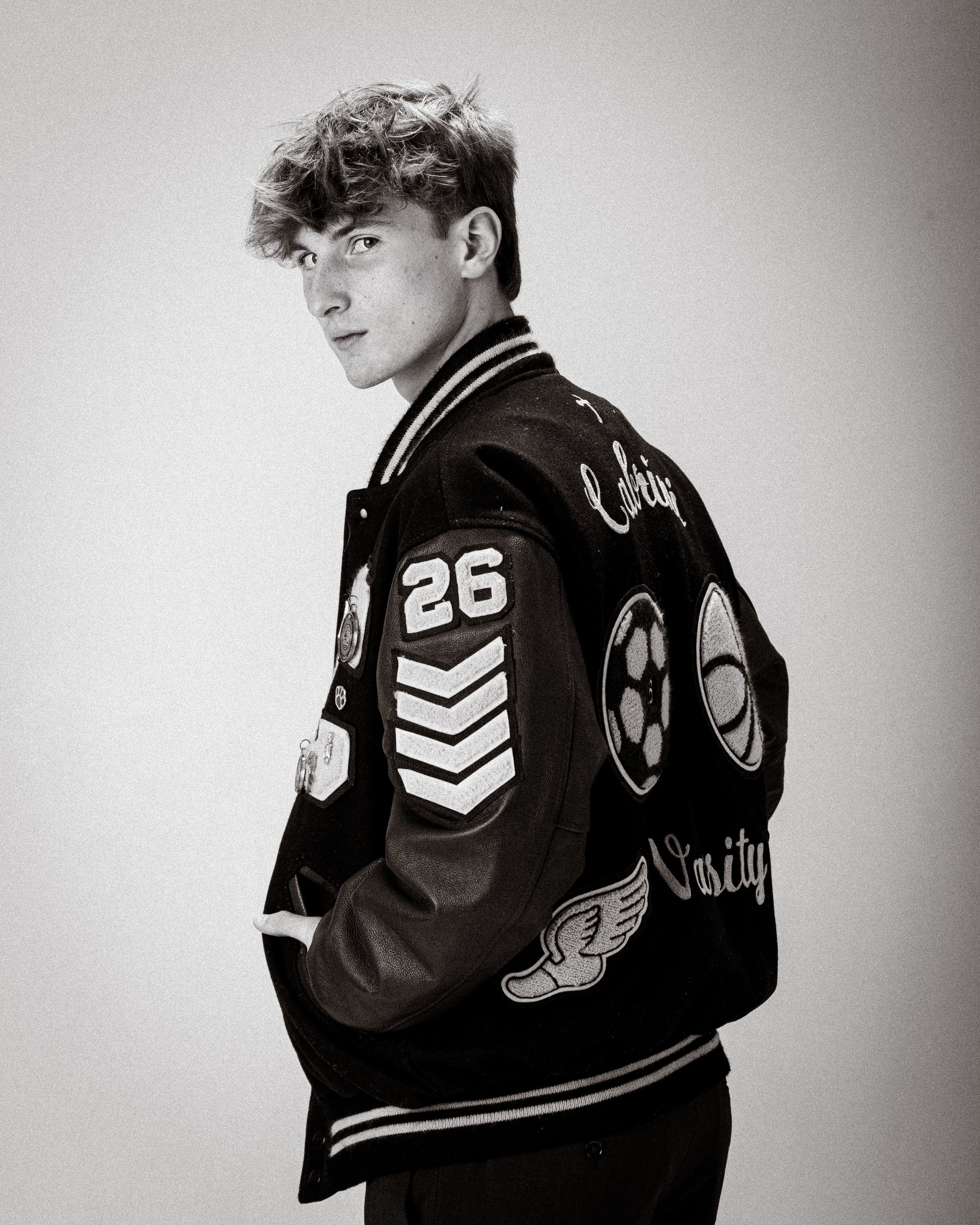 Cabrini High senior Brad posing with a varsity backpack featuring sports logos and 'Laborini' text, showcasing school spirit in a minimalist studio setting.