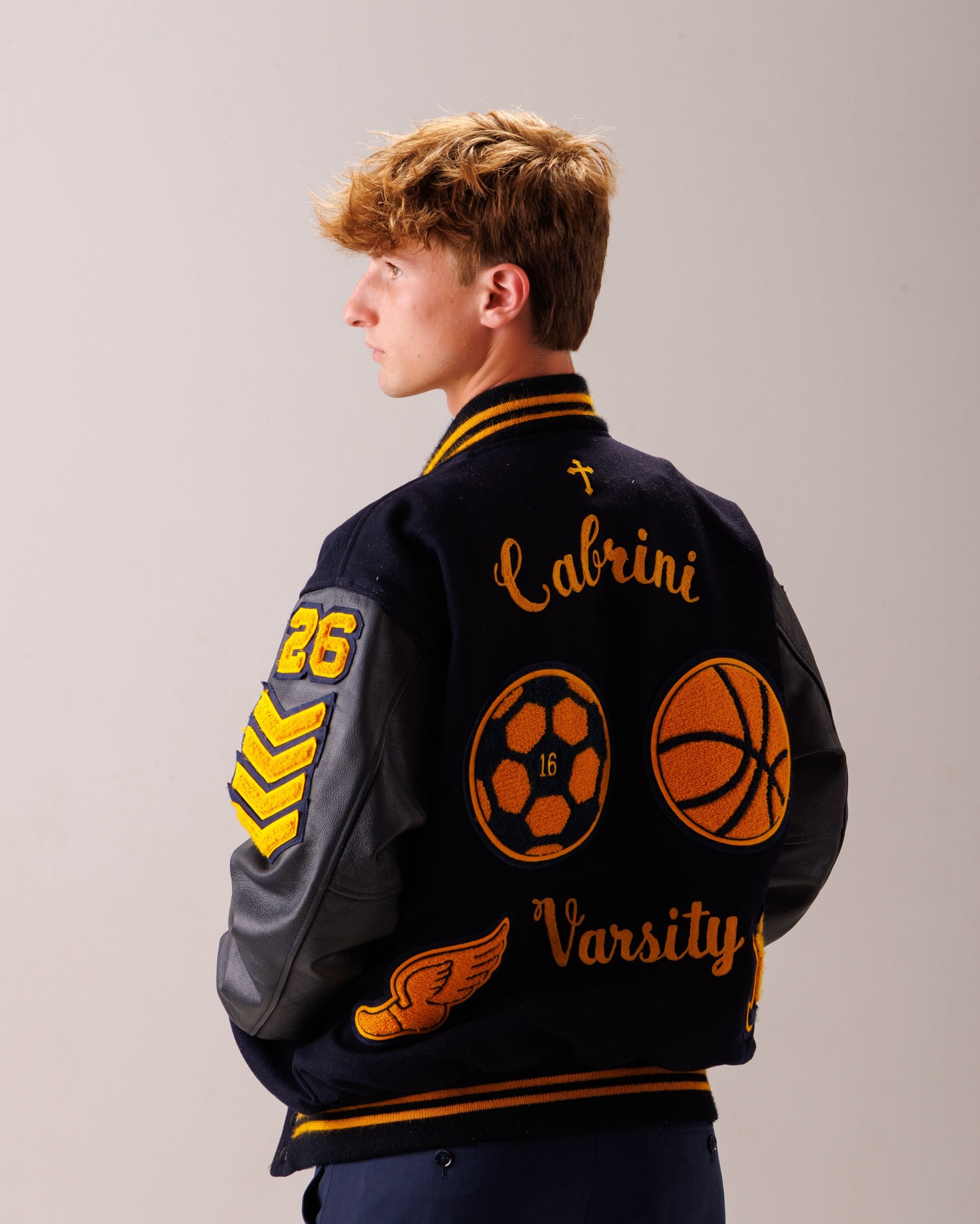 Cabrini High senior Brad posing with a varsity backpack featuring sports logos and 'Laborini' text, showcasing school spirit in a minimalist studio setting.