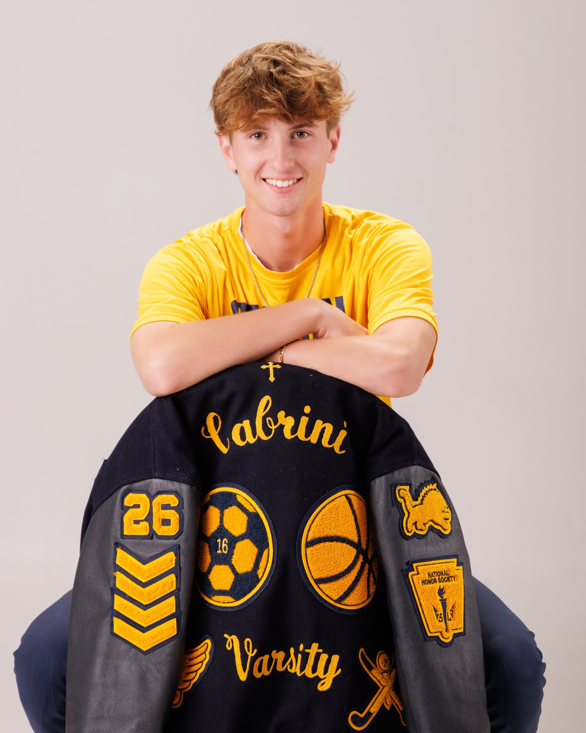 Cabrini High senior Brad posing with a varsity backpack featuring sports logos and 'Laborini' text, showcasing school spirit in a minimalist studio setting.