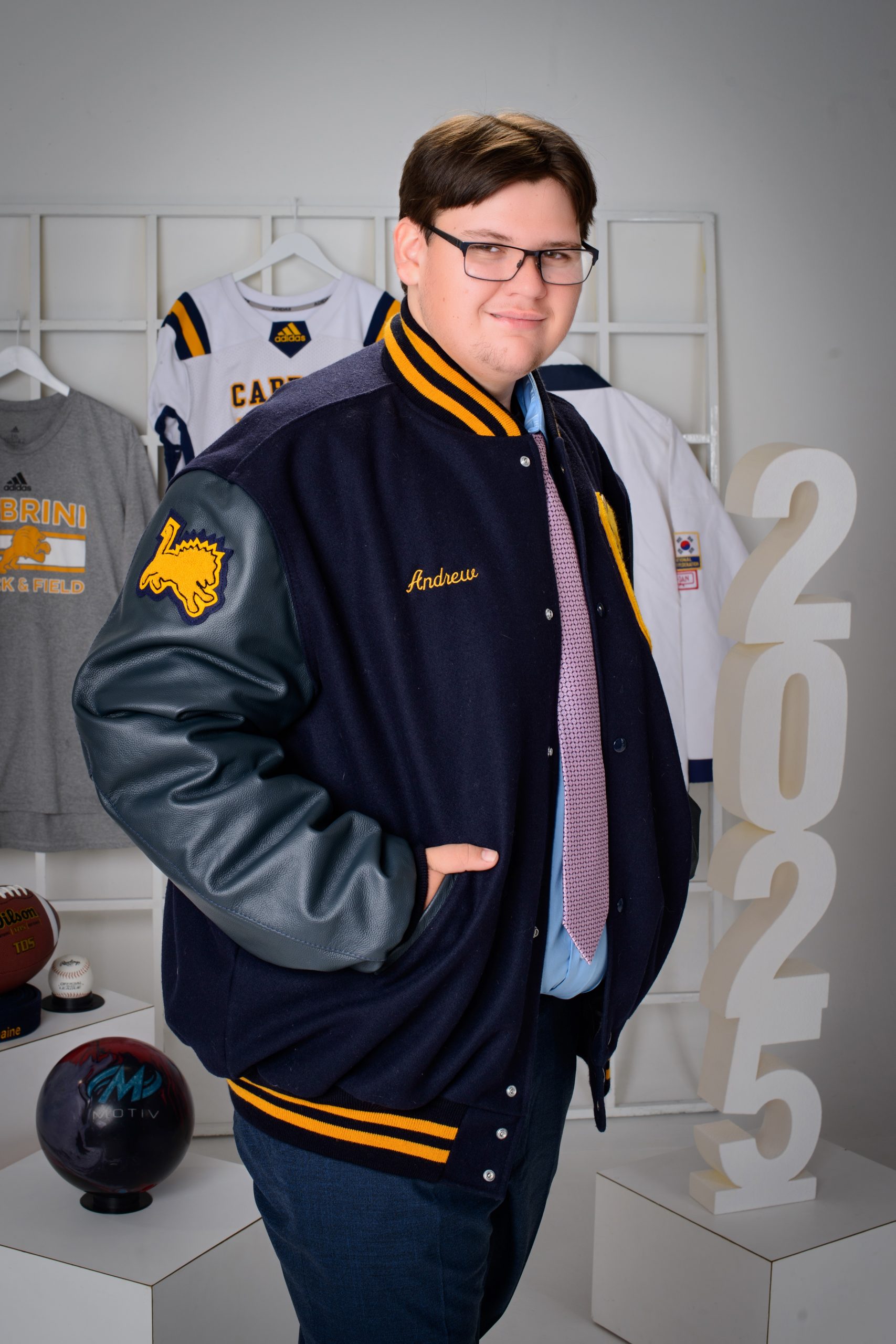 Andrew wearing a custom 'Cabrini' varsity jacket with his name embroidered, standing beside '2025' numerals