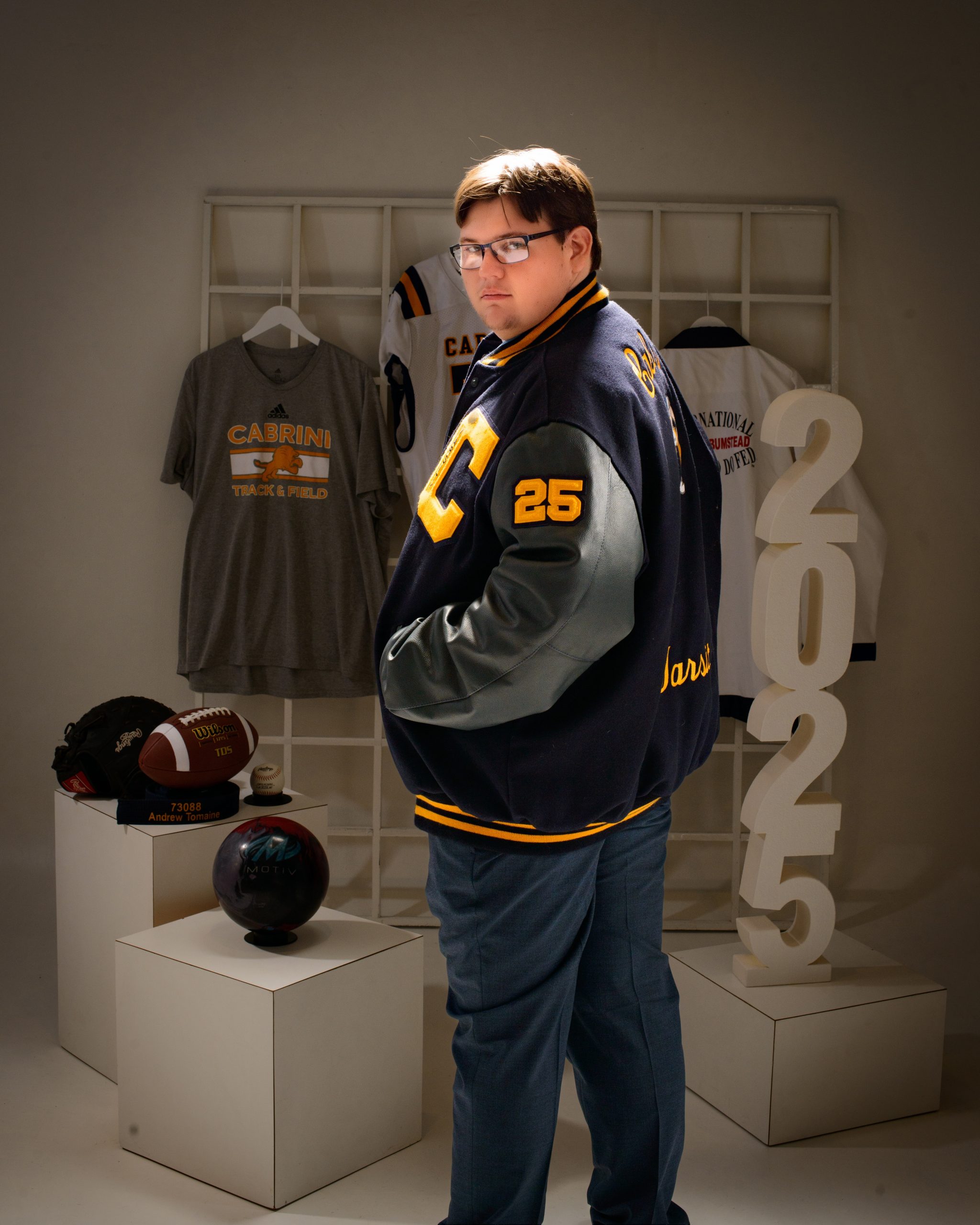 Andrew posing in a Cabrini-themed jacket and pants set, surrounded by sports gear and school logos