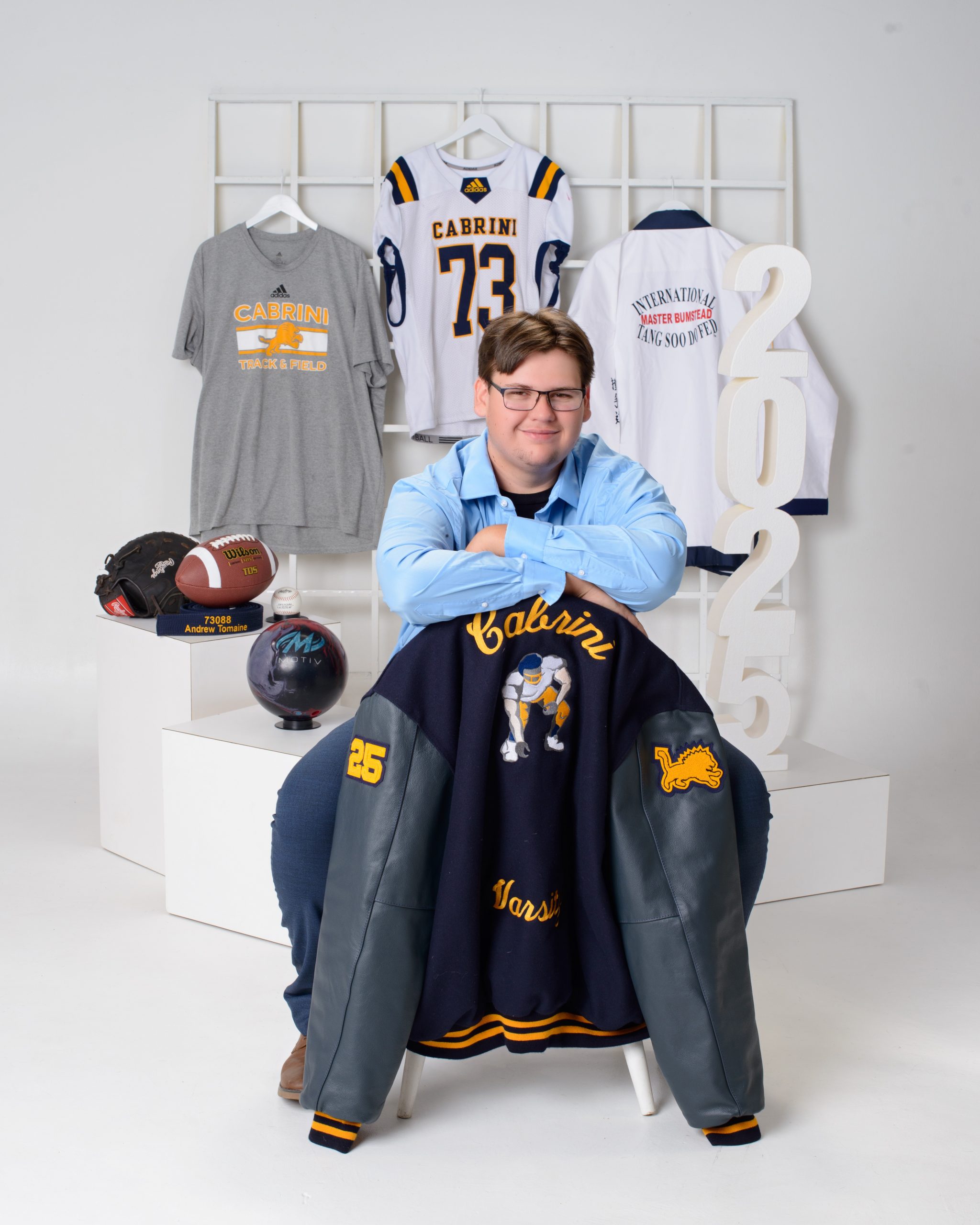 Andrew posing in a Cabrini-themed jacket and pants set, surrounded by sports gear and school logos