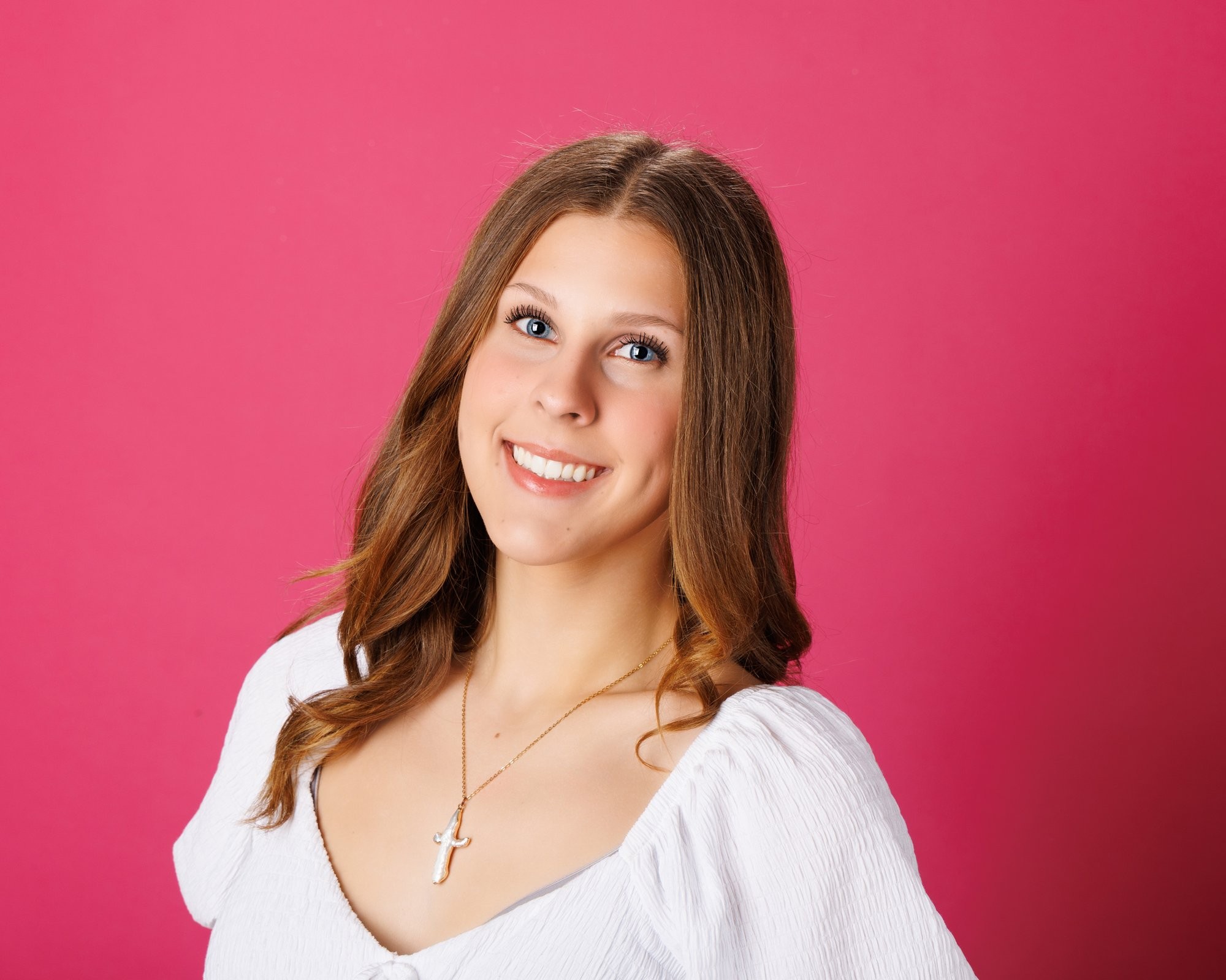 Cabrini Senior student Isabella's vibrant pink mosaic background portrait, white blouse, and cross necklace