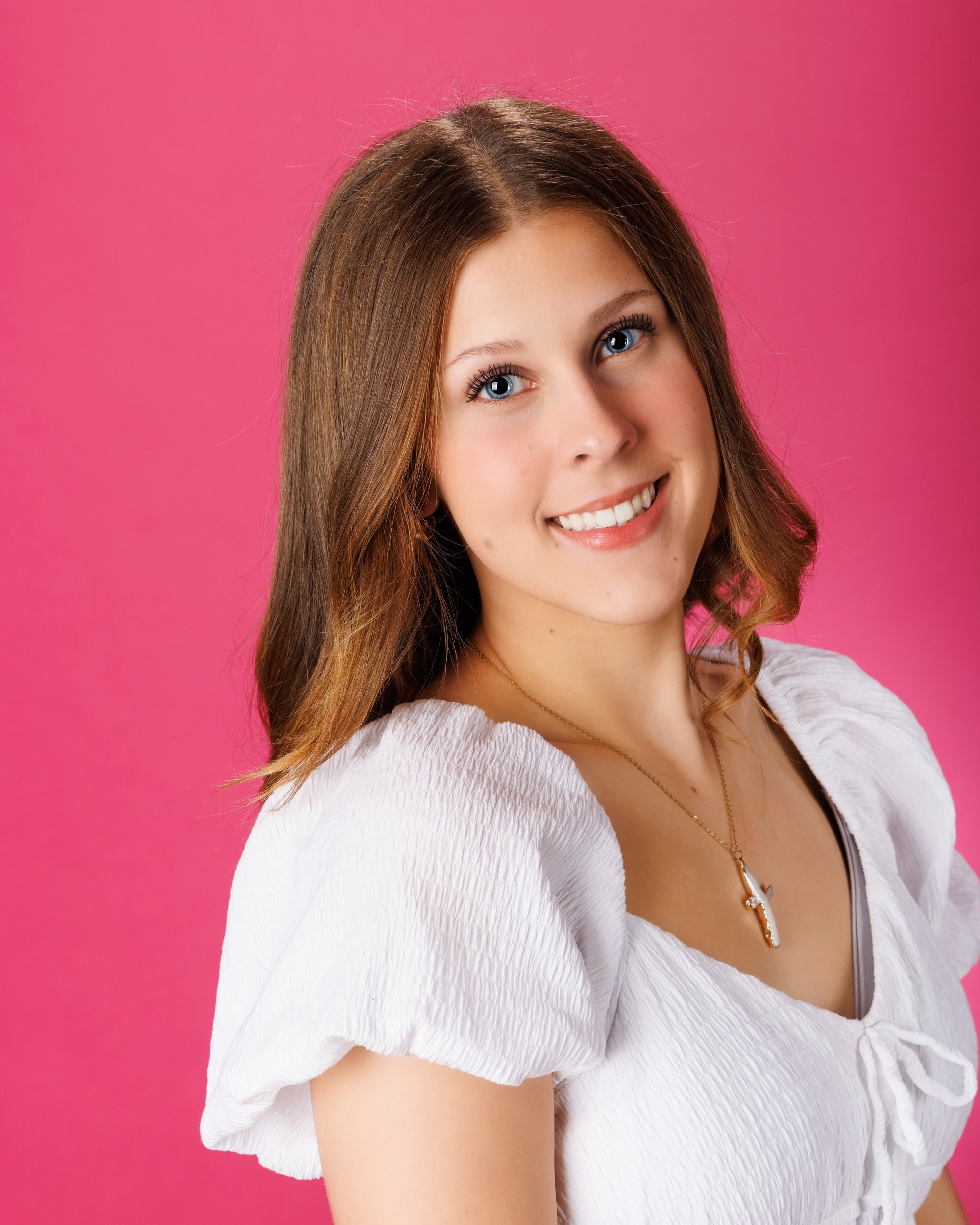 Cabrini Senior student Isabella's vibrant pink mosaic background portrait, white blouse, and cross necklace