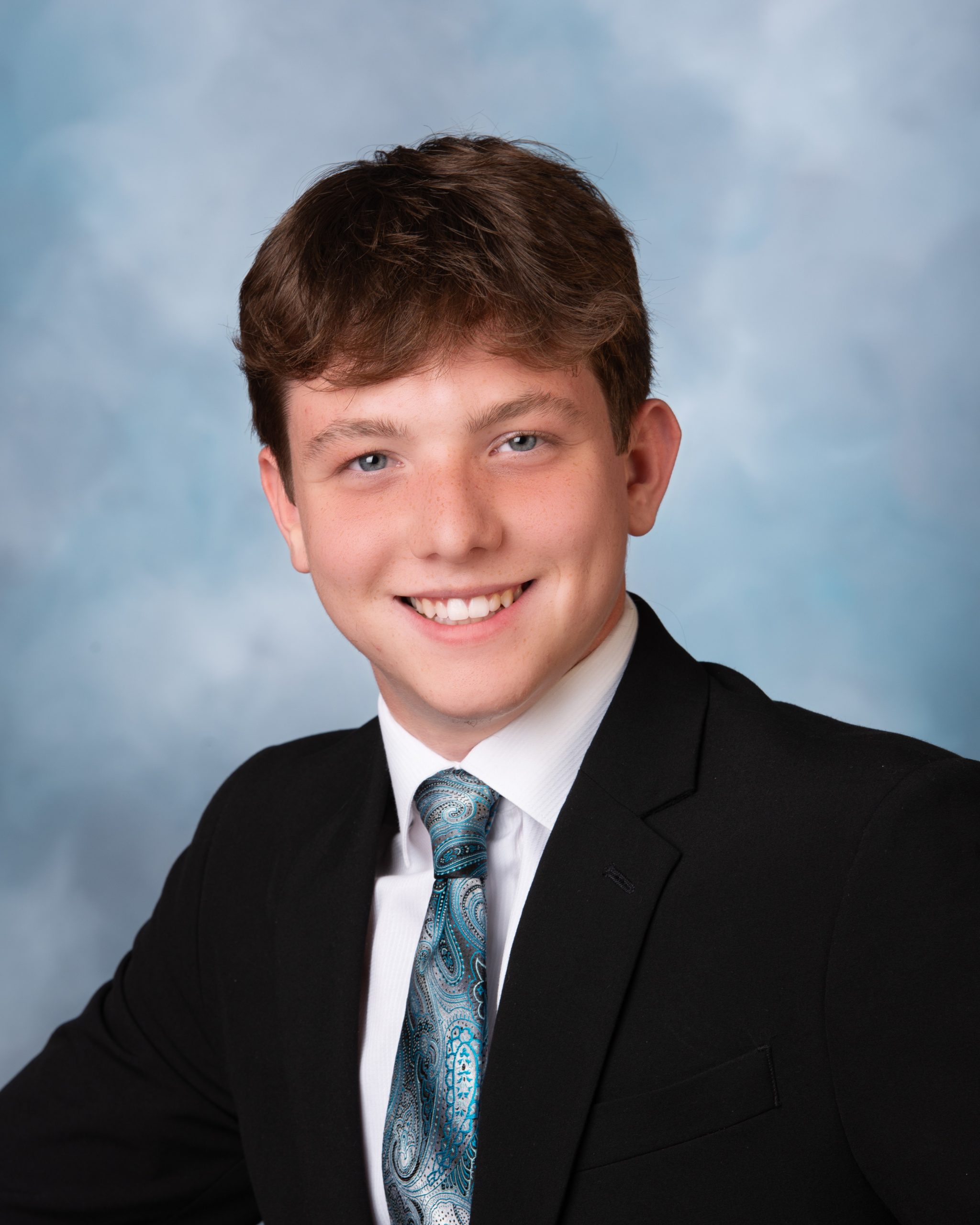 Senior headshot of Wyatt in black suit and blue tie against soft blue backdrop