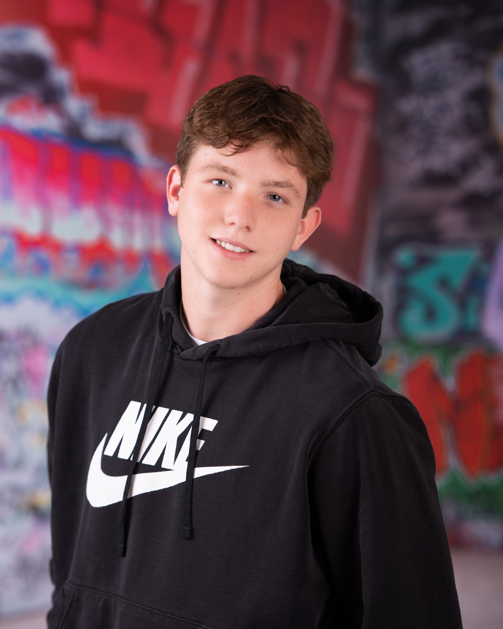 Wyatt in black Nike hoodie with graffiti art backdrop for senior photography session