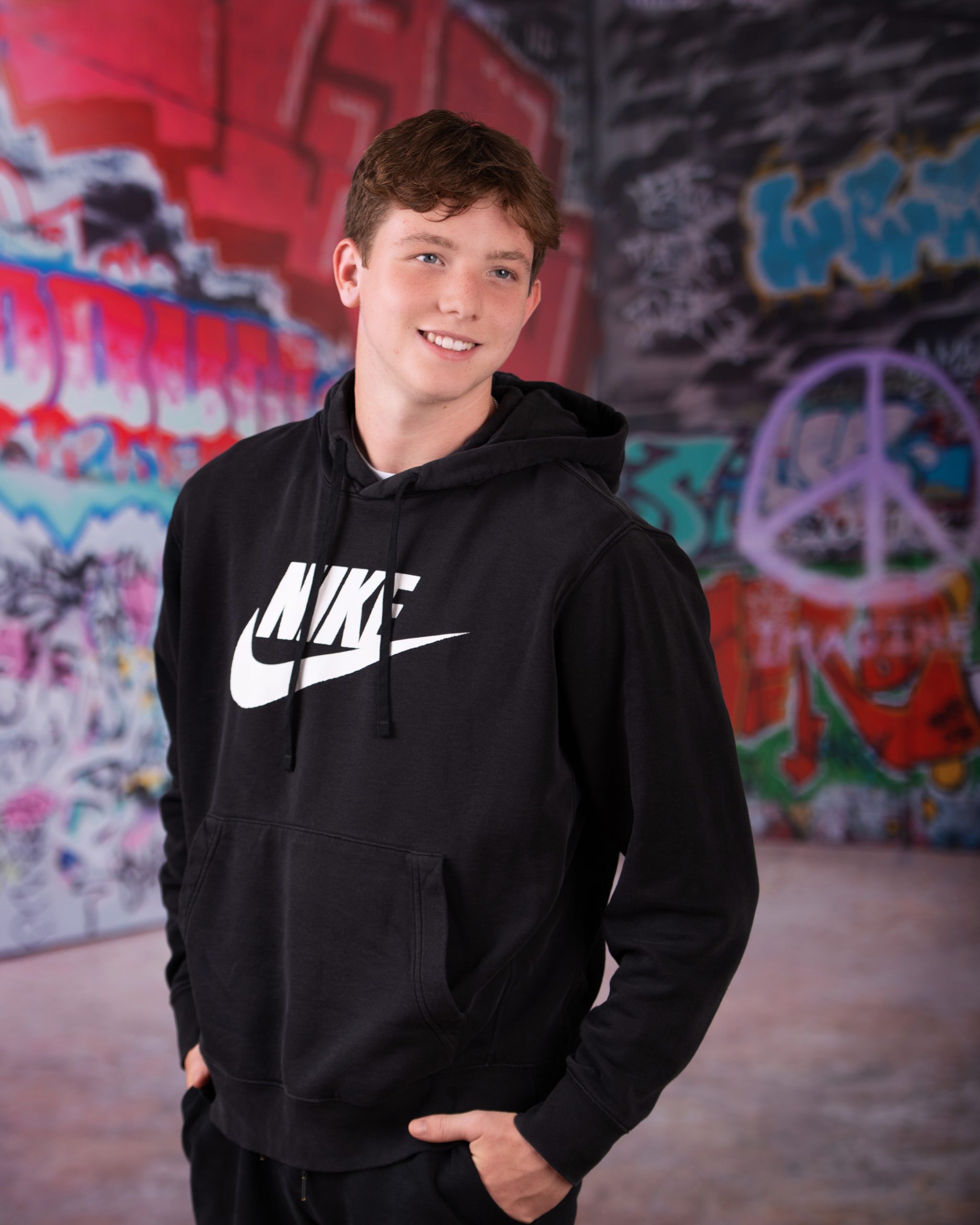 Wyatt in black Nike hoodie with graffiti art backdrop for senior photography session