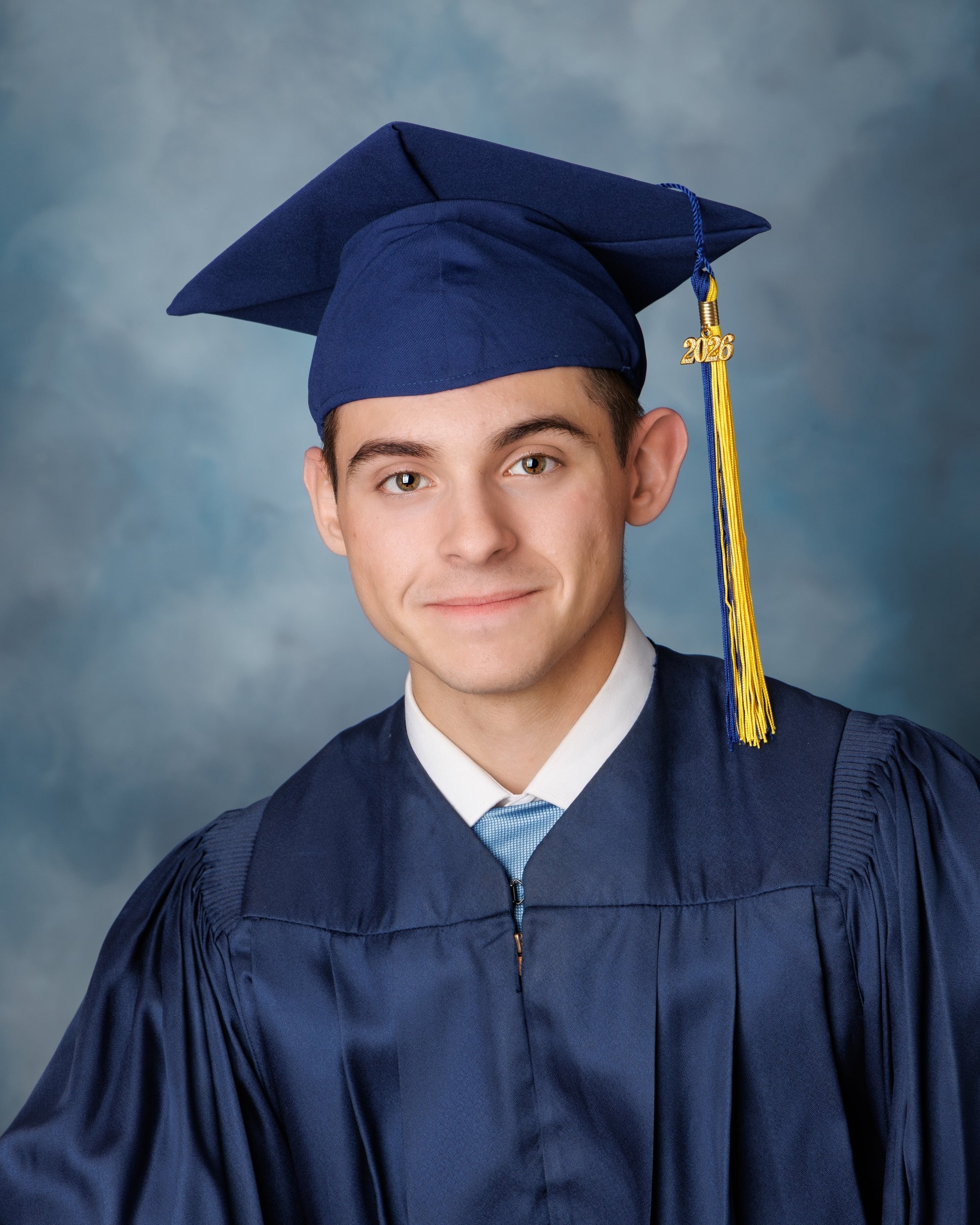 Senior portrait of a young adult in black zip-up and green tie standing against textured stone wall.