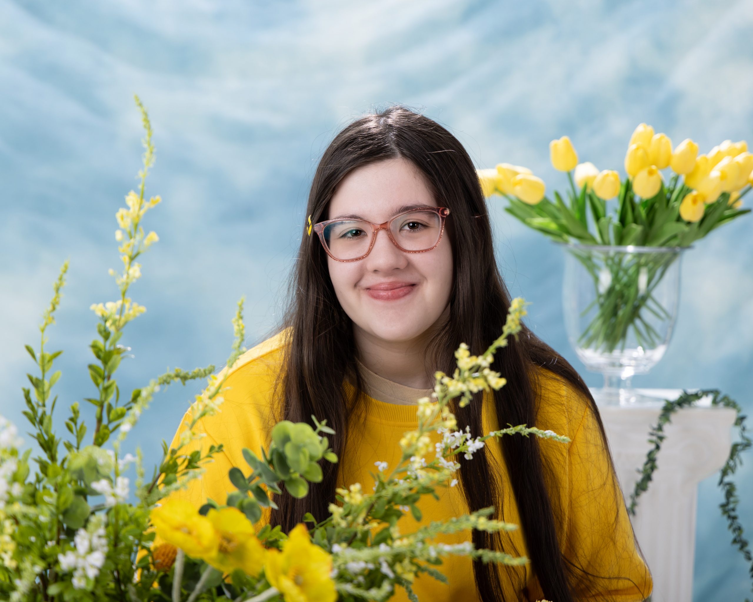 Anna in yellow sweater with tulips against blue backdrop, studio senior portrait