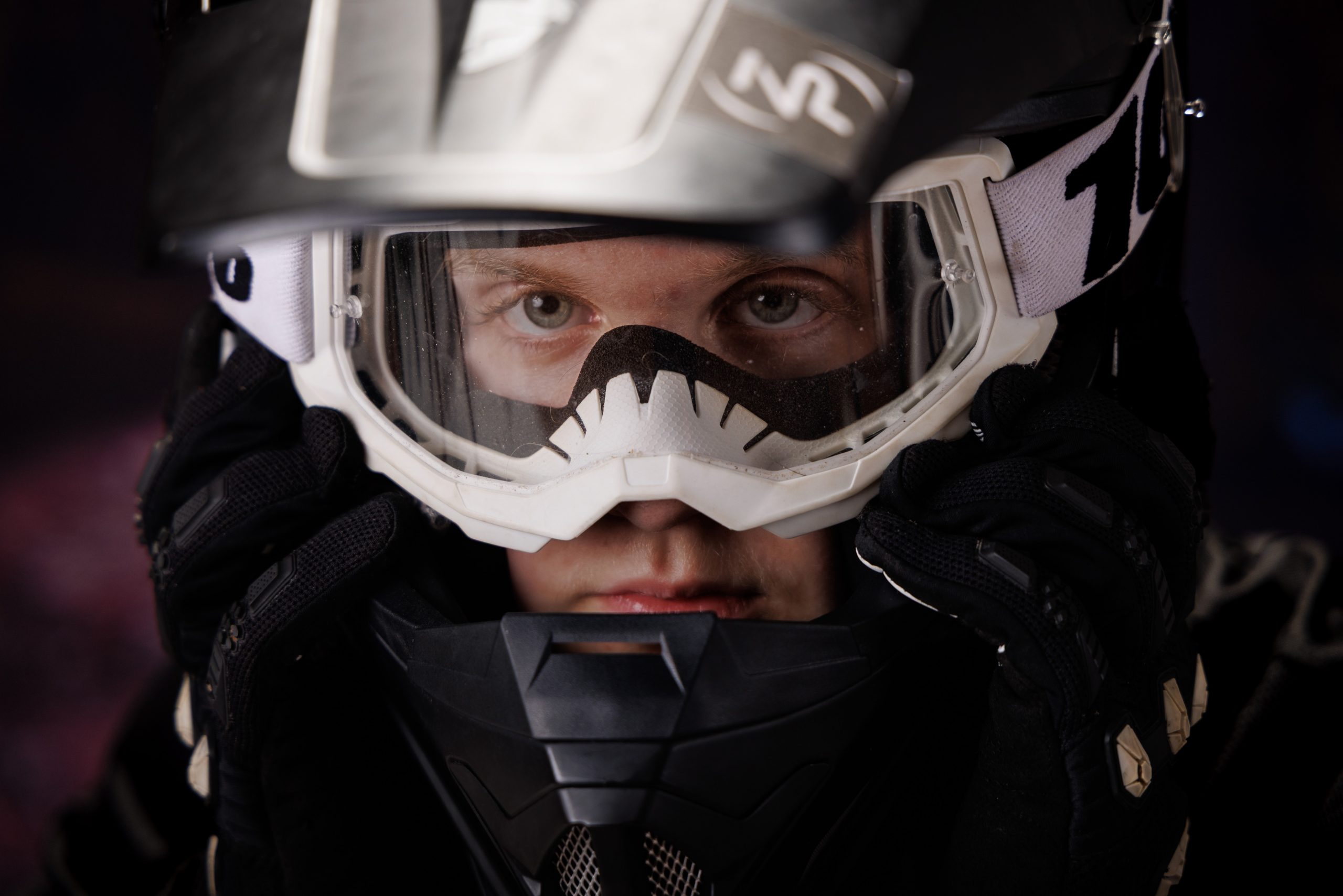 A senior holds a motorcross helmet and goggles while standing against a vibrant, peeling wall backdrop