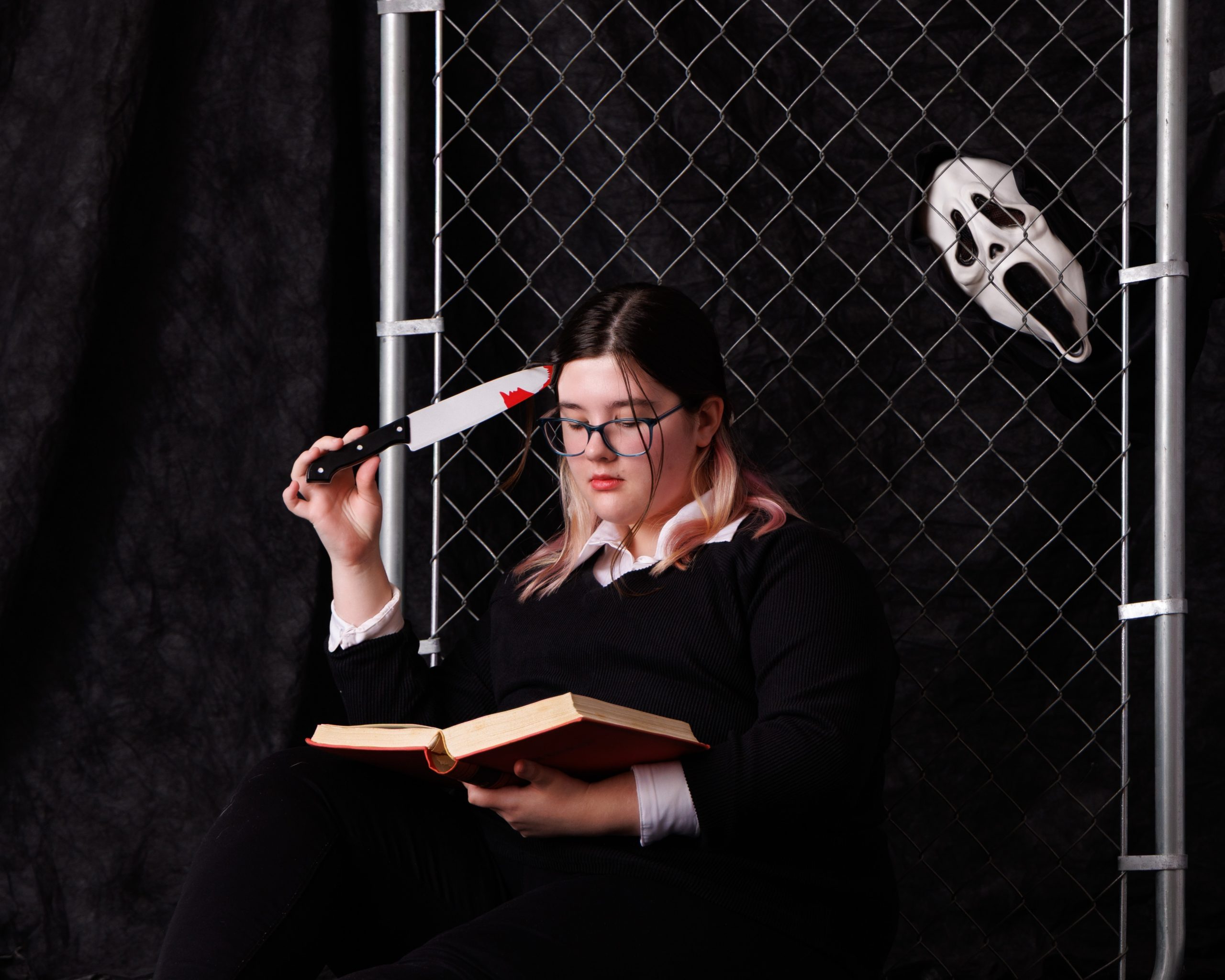 Kaitlyn posing with horror-themed props including a knife and book in a studio setup for her Canton Plymouth senior session