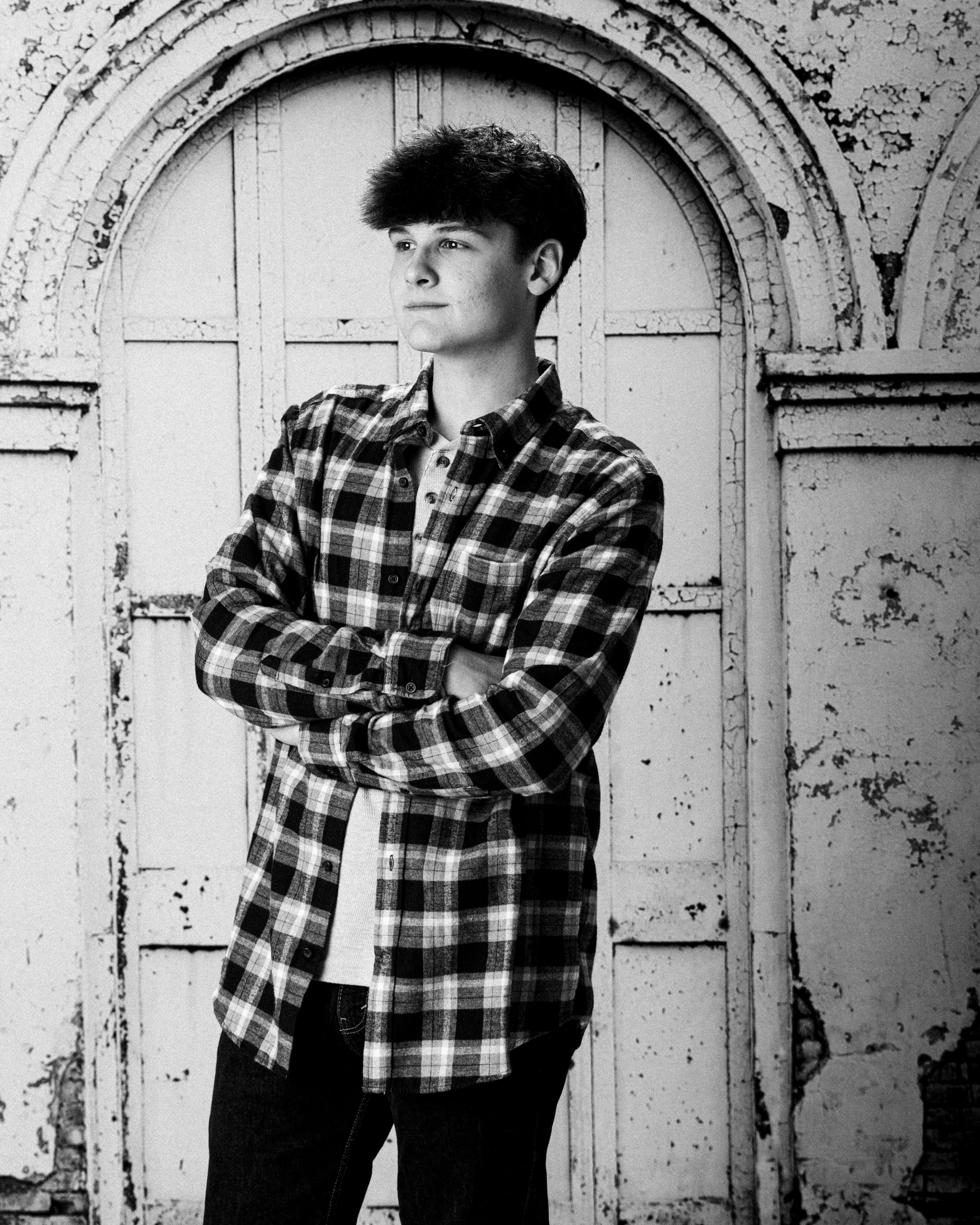 Senior portrait of Andrew standing with arms crossed in front of an arched door