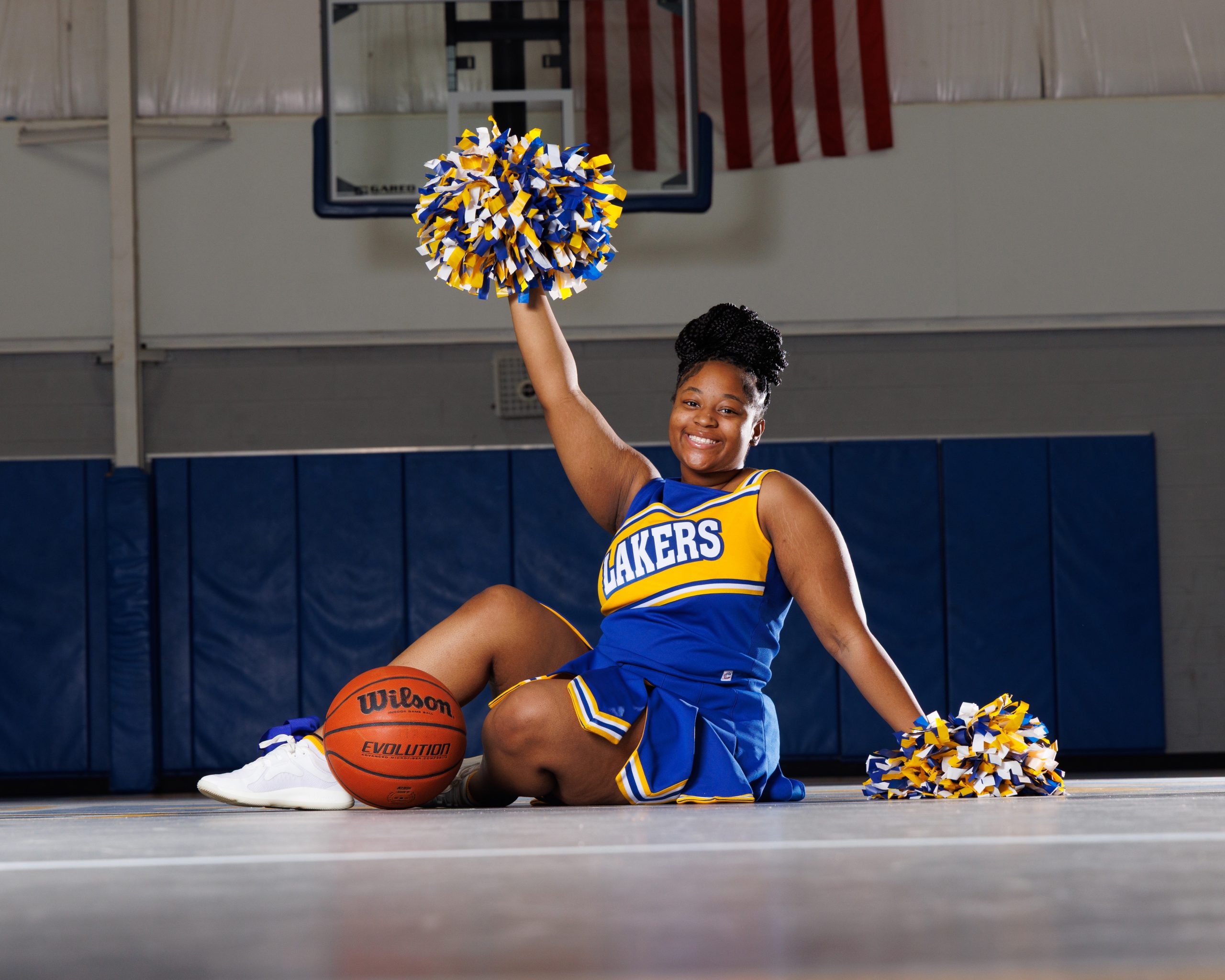 Cheerleader standing on basketball with pom-poms, showcasing team spirit in Detroit high school sports portraits