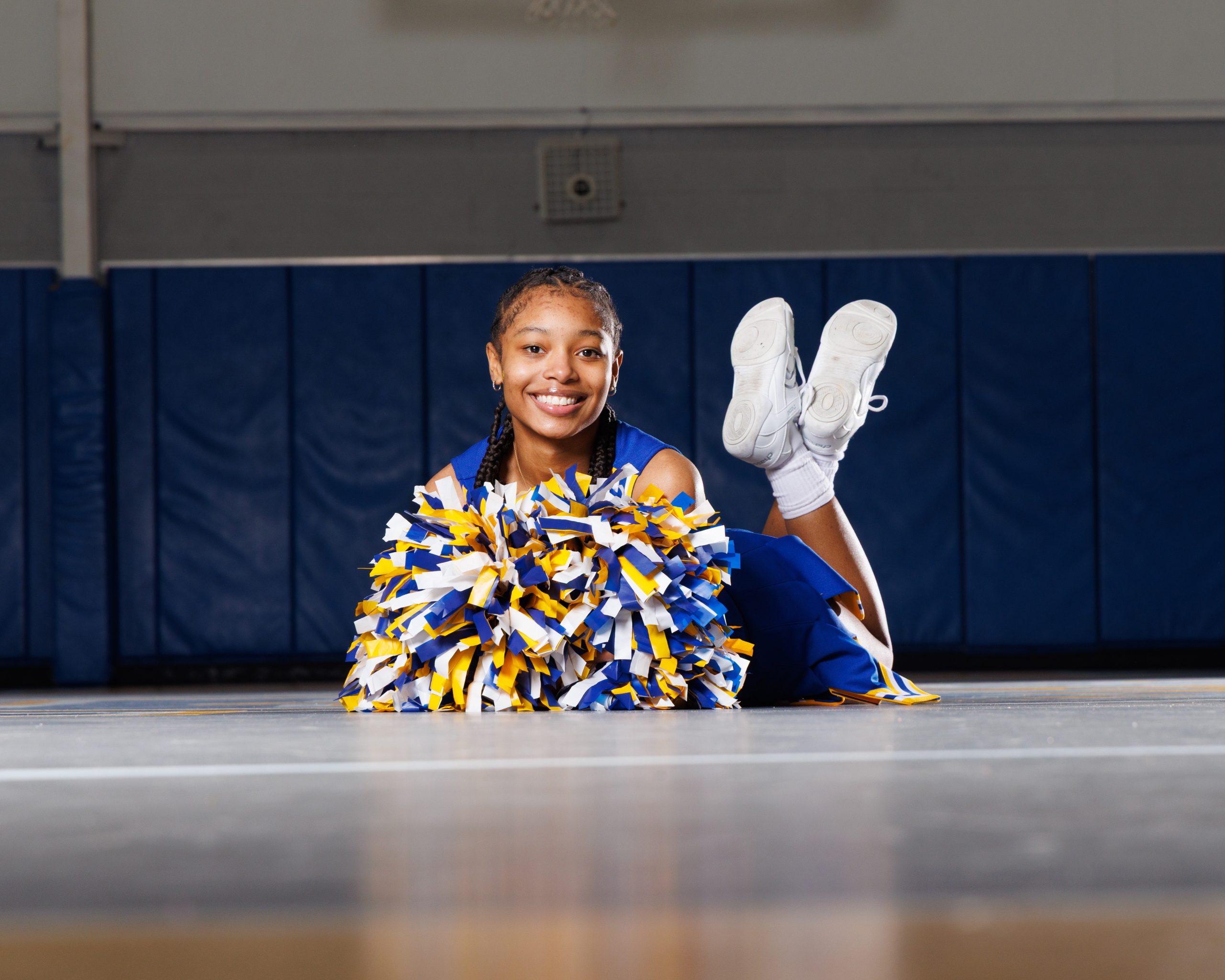 Cheerleader standing on basketball with pom-poms, showcasing team spirit in Detroit high school sports portraits