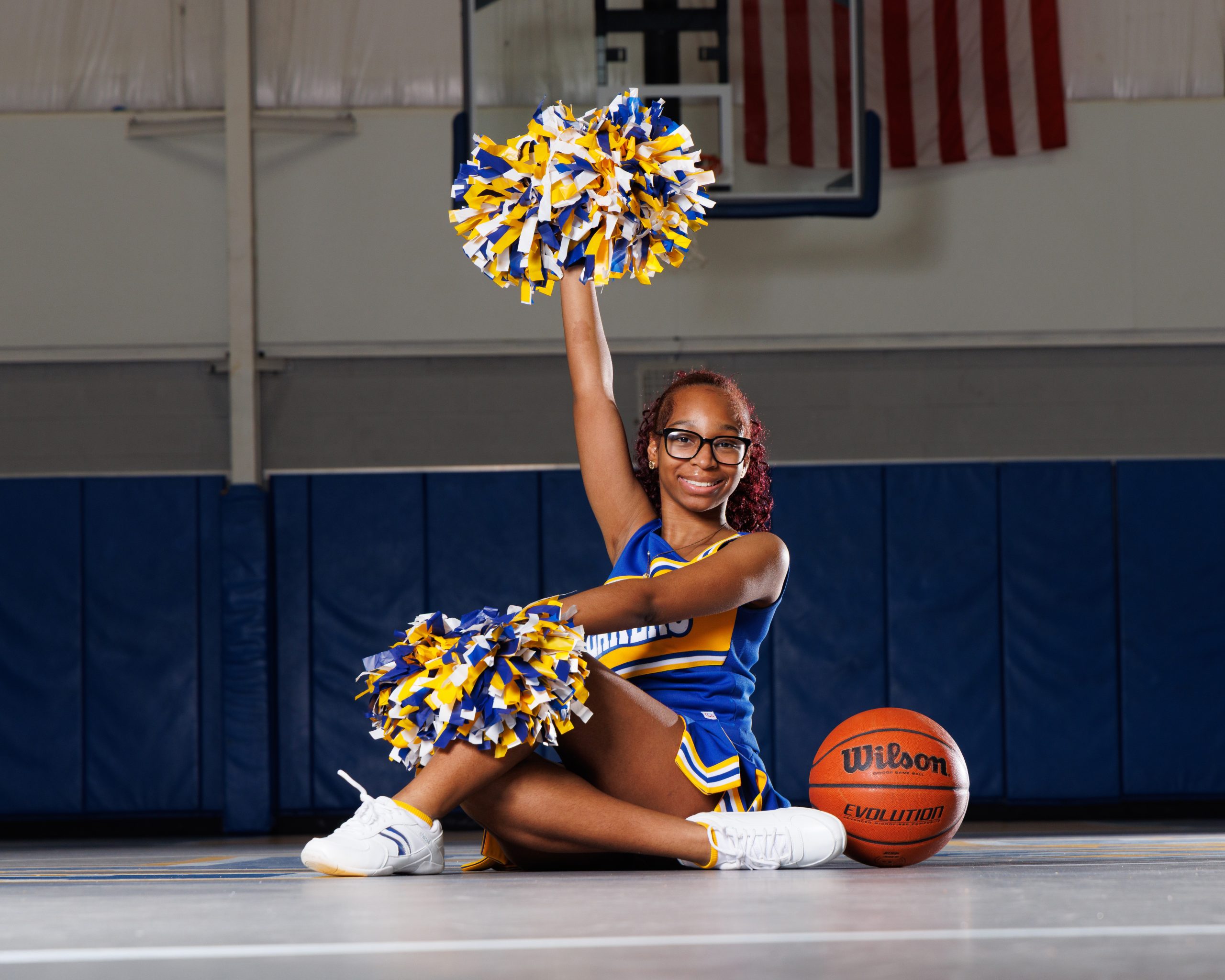Cheerleader standing on basketball with pom-poms, showcasing team spirit in Detroit high school sports portraits
