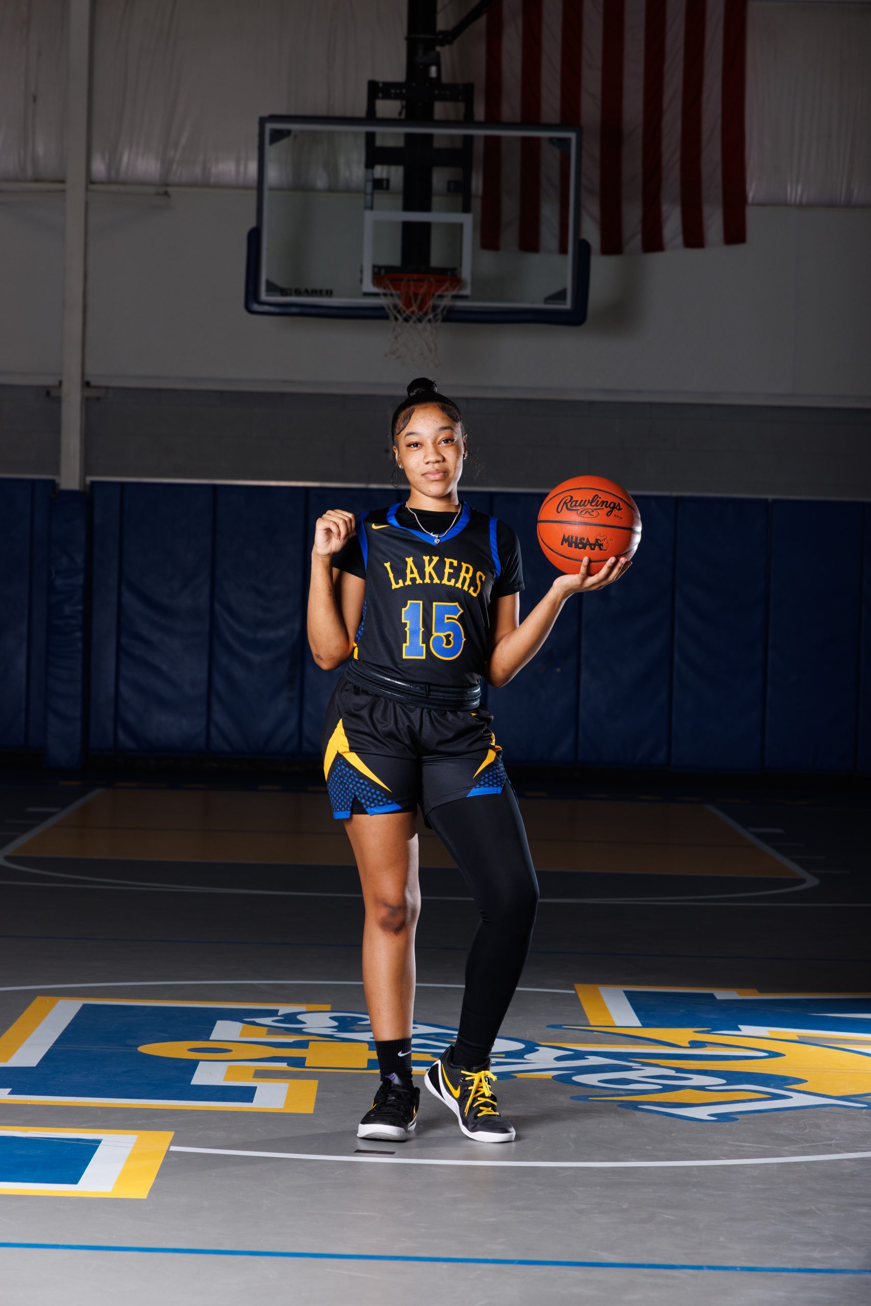 Cheerleader standing on basketball with pom-poms, showcasing team spirit in Detroit high school sports portraits