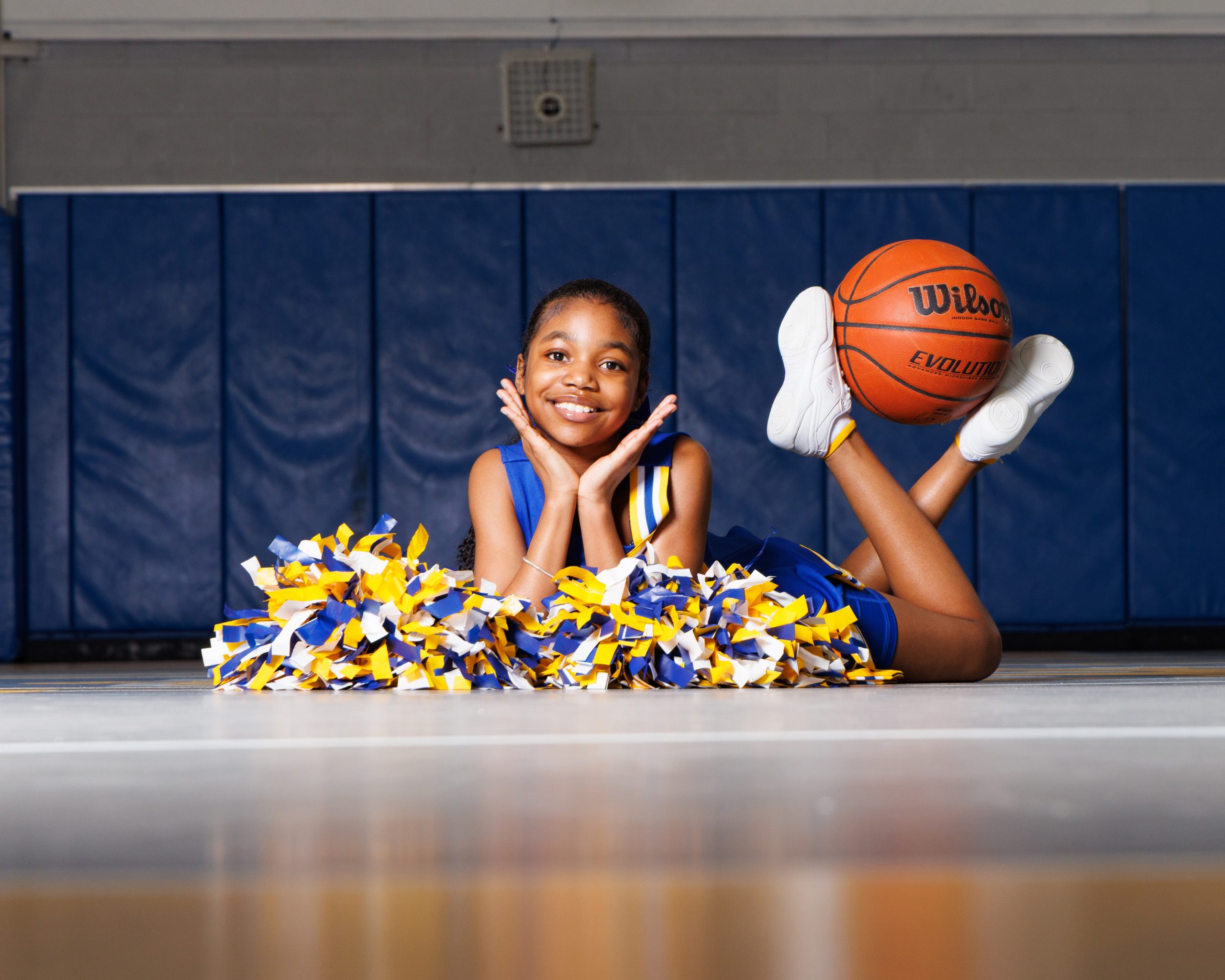 Cheerleader standing on basketball with pom-poms, showcasing team spirit in Detroit high school sports portraits