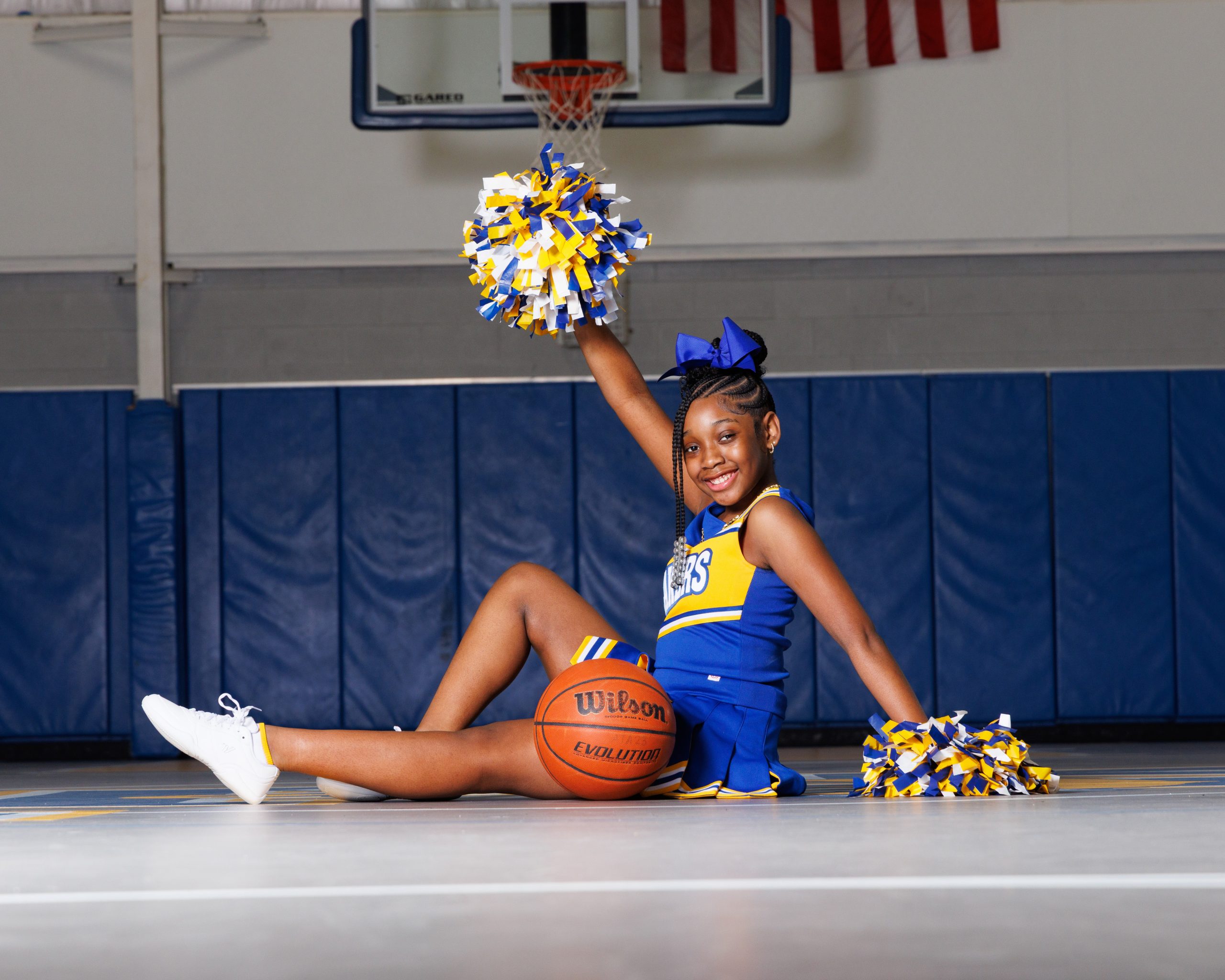Cheerleader standing on basketball with pom-poms, showcasing team spirit in Detroit high school sports portraits