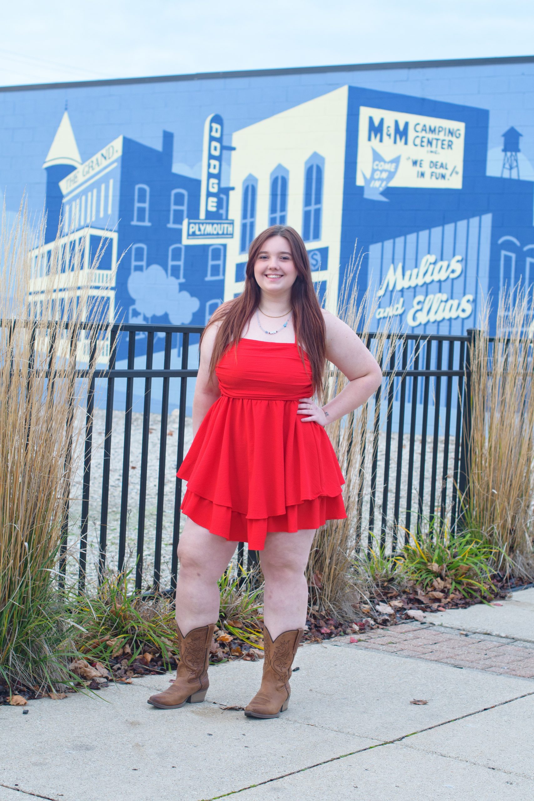 High school student smiling in red dress against a blue cityscape backdrop for Downriver senior photography