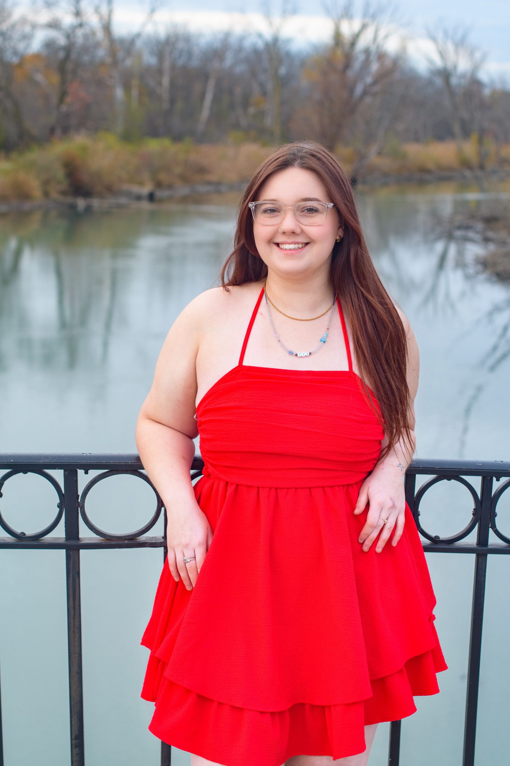 High school student smiling in red dress against a blue cityscape backdrop for Downriver senior photography