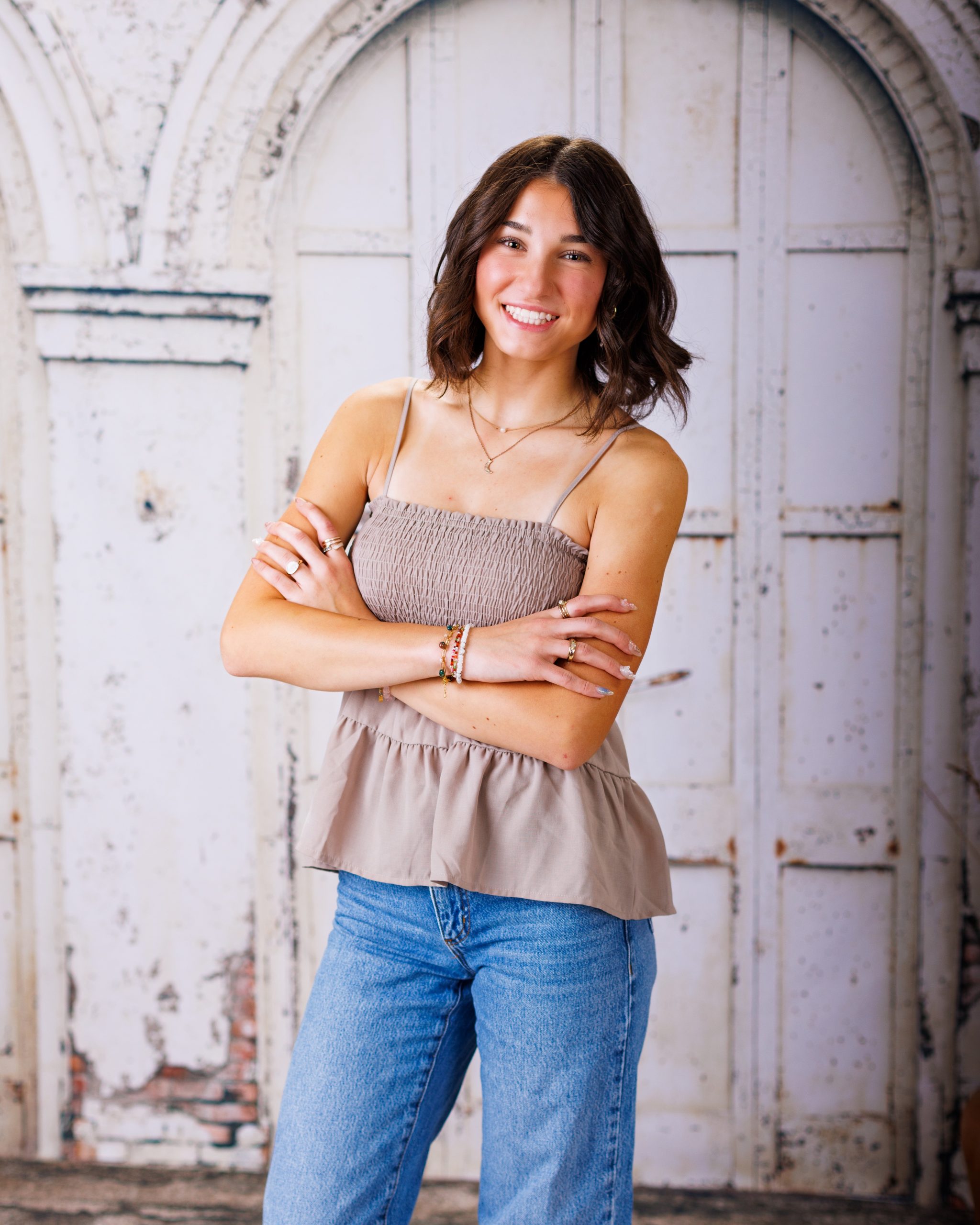Anna poses with arms crossed against a rustic white door background for senior photography session