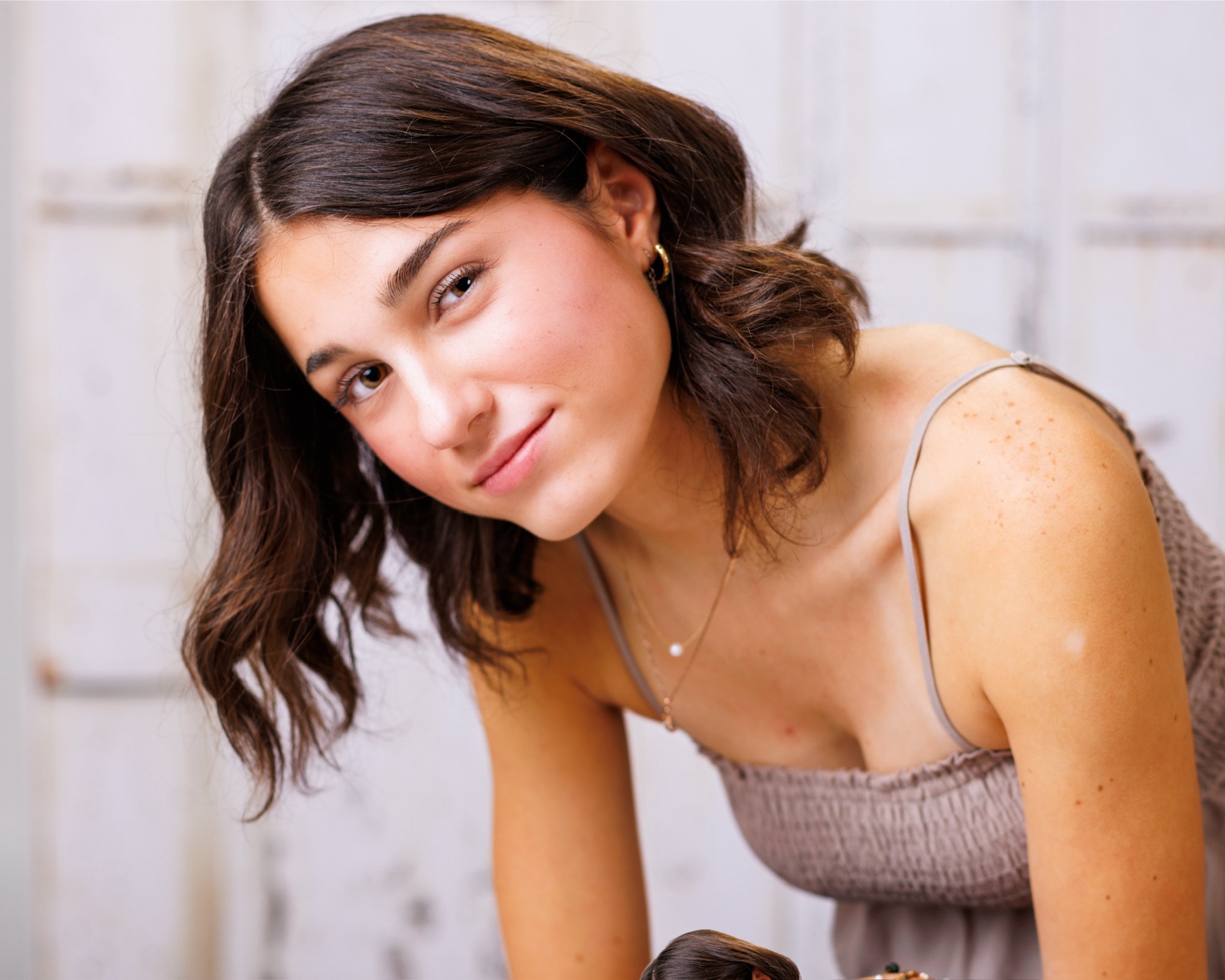 Anna poses with arms crossed against a rustic white door background for senior photography session