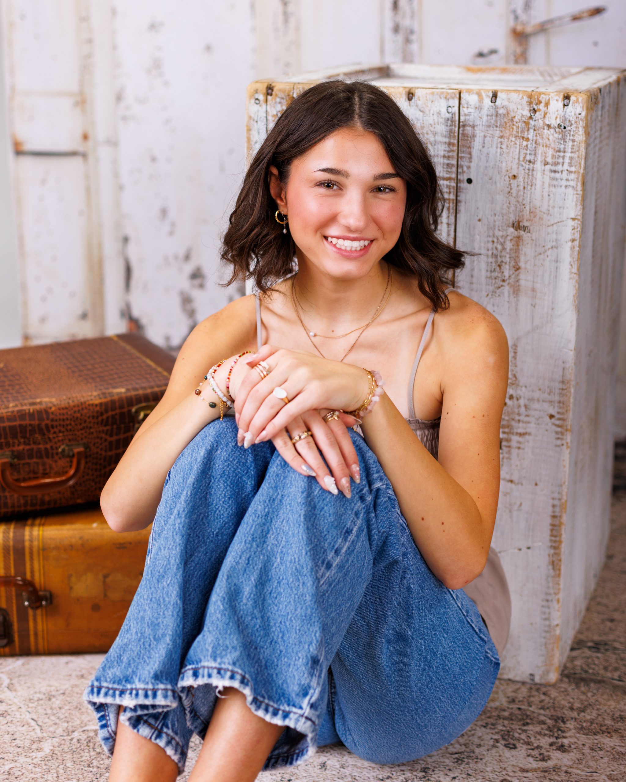 Anna poses with arms crossed against a rustic white door background for senior photography session