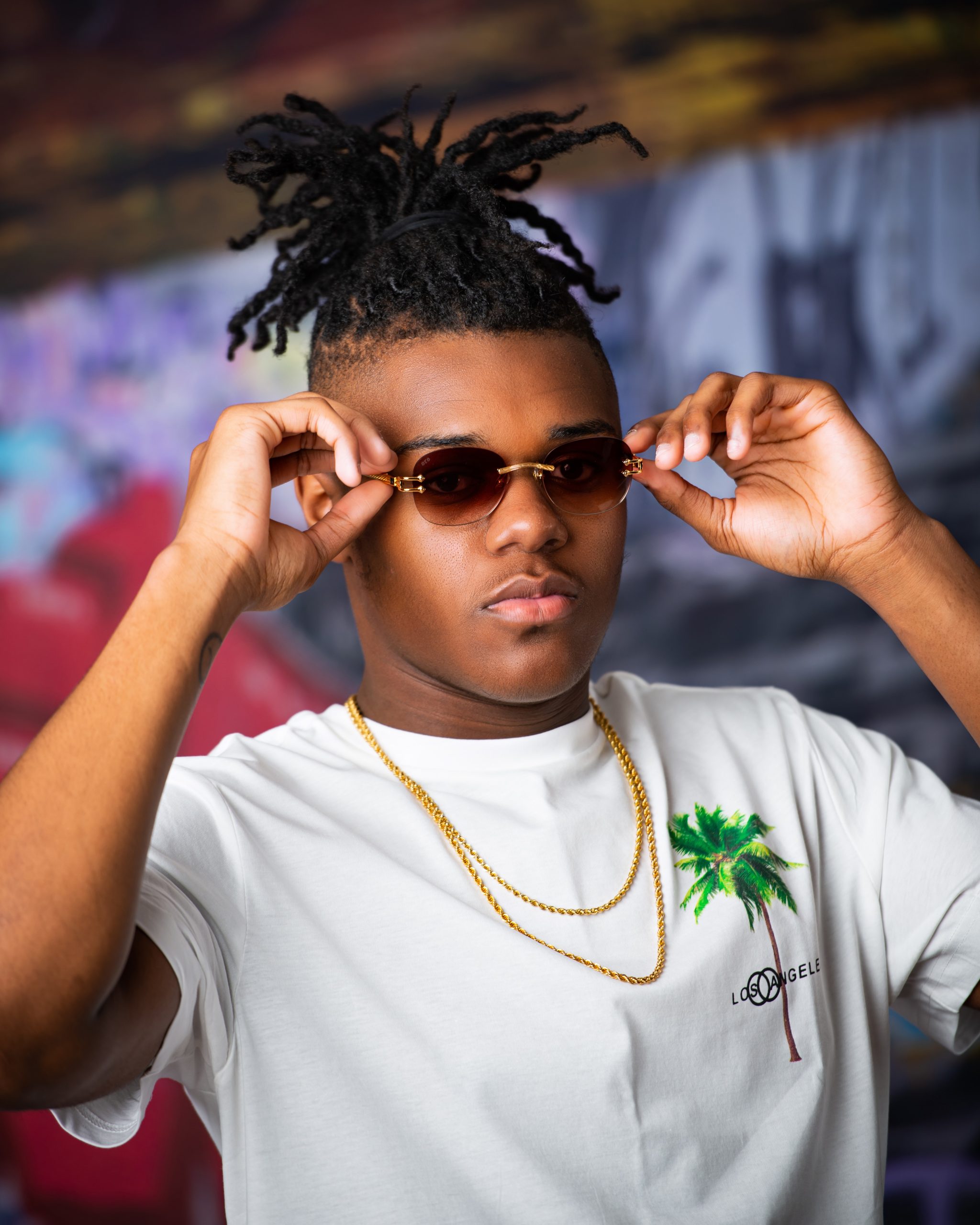 Frederick wearing graduation cap and sneakers on graffiti wall in studio session