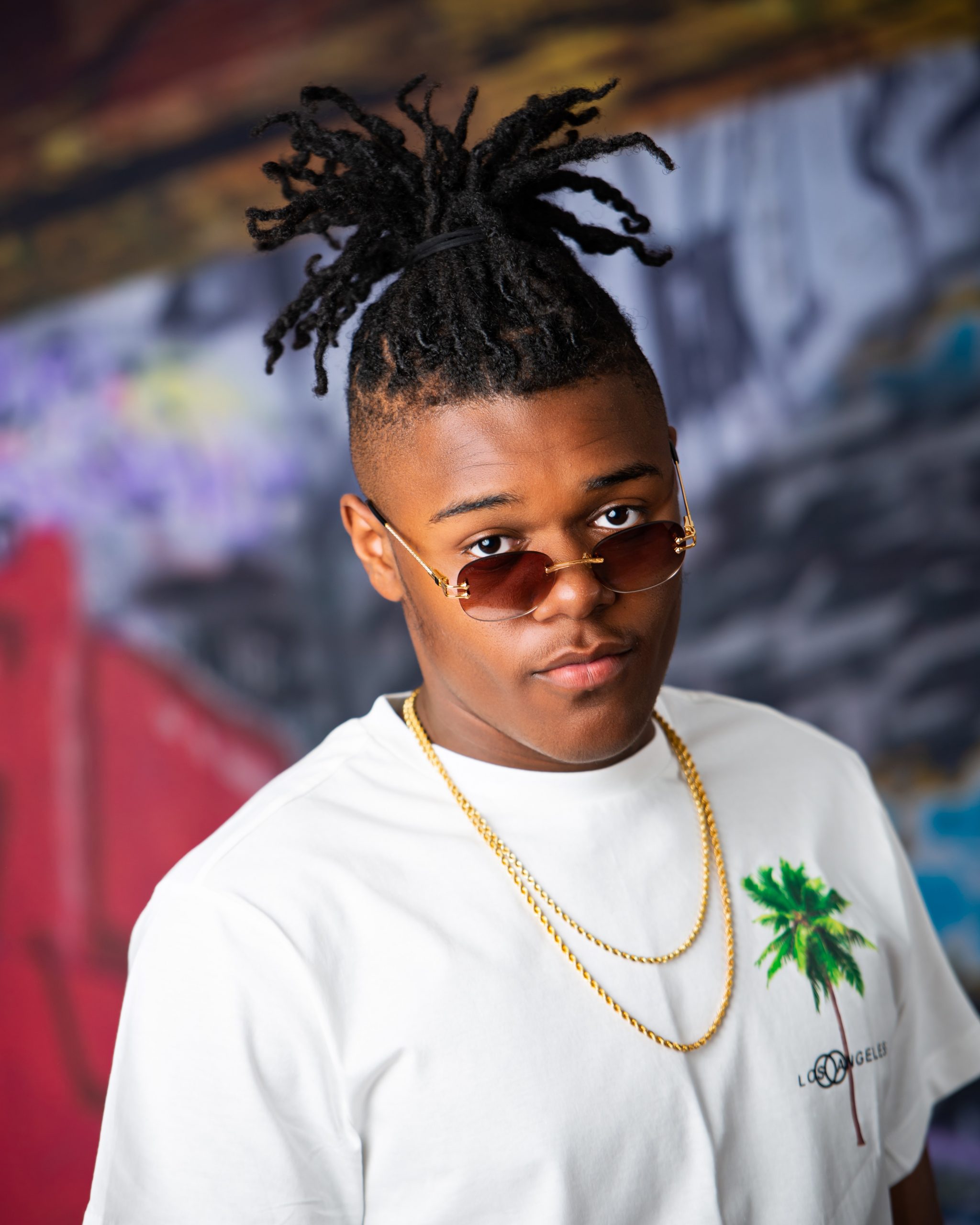 Frederick wearing graduation cap and sneakers on graffiti wall in studio session