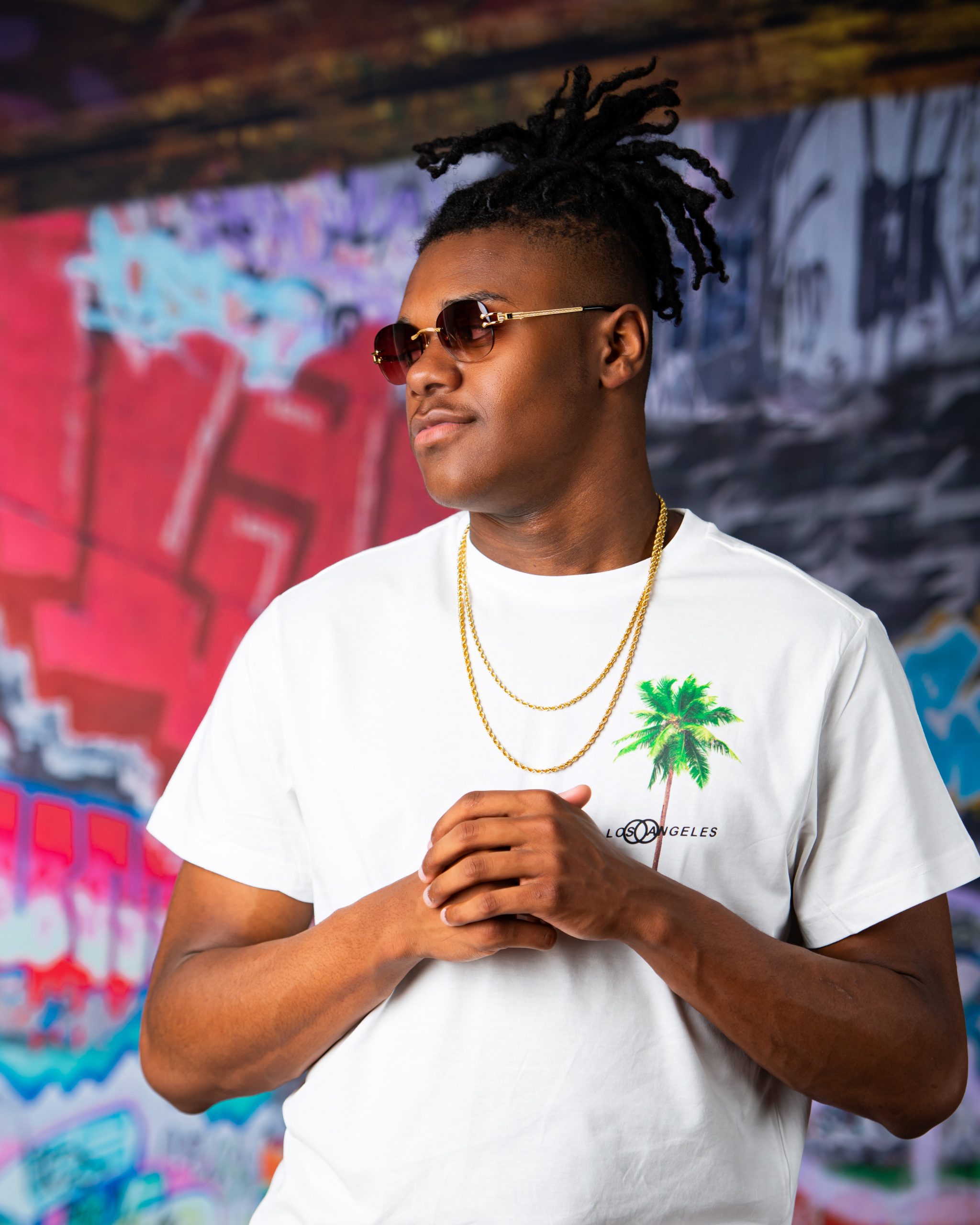 Frederick wearing graduation cap and sneakers on graffiti wall in studio session