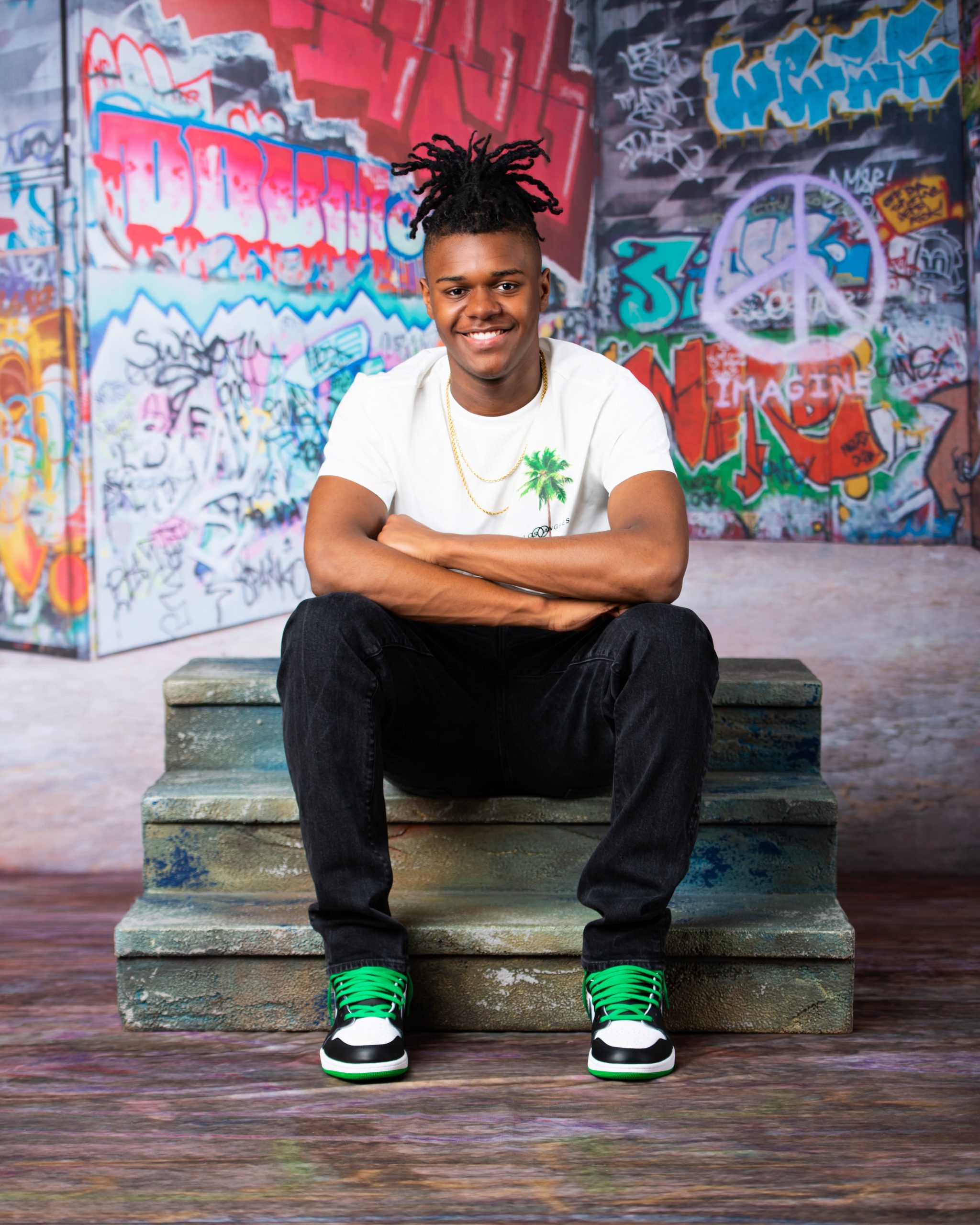 Frederick wearing graduation cap and sneakers on graffiti wall in studio session