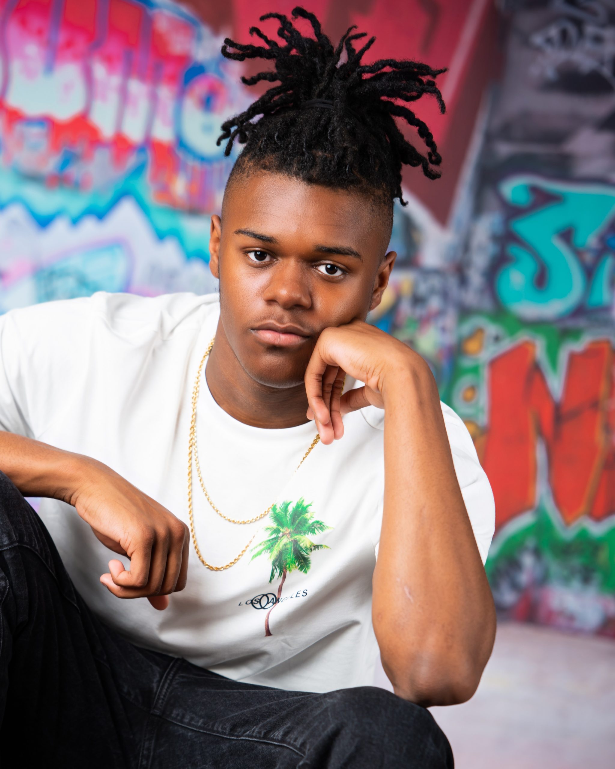 Frederick wearing graduation cap and sneakers on graffiti wall in studio session