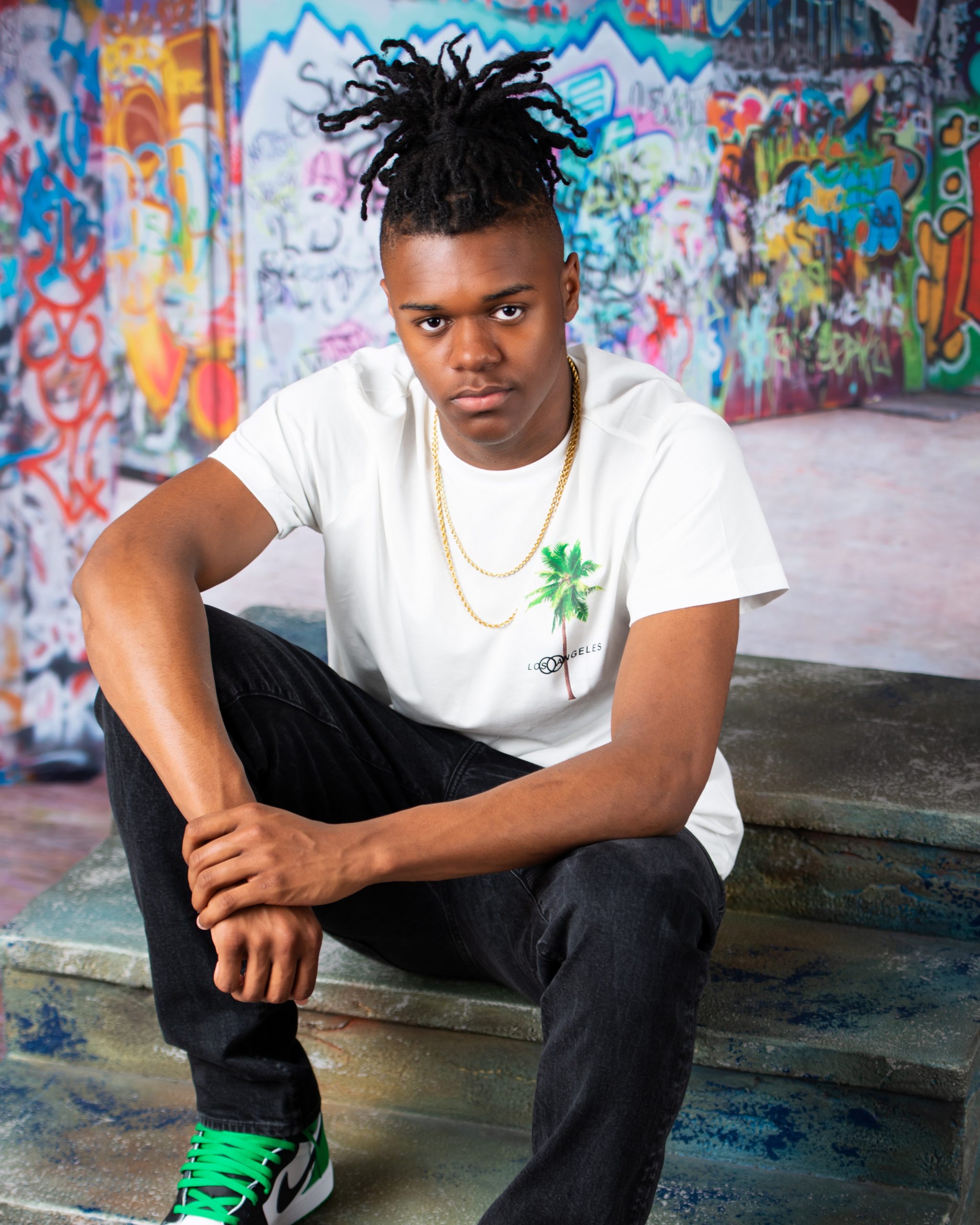 Frederick wearing graduation cap and sneakers on graffiti wall in studio session