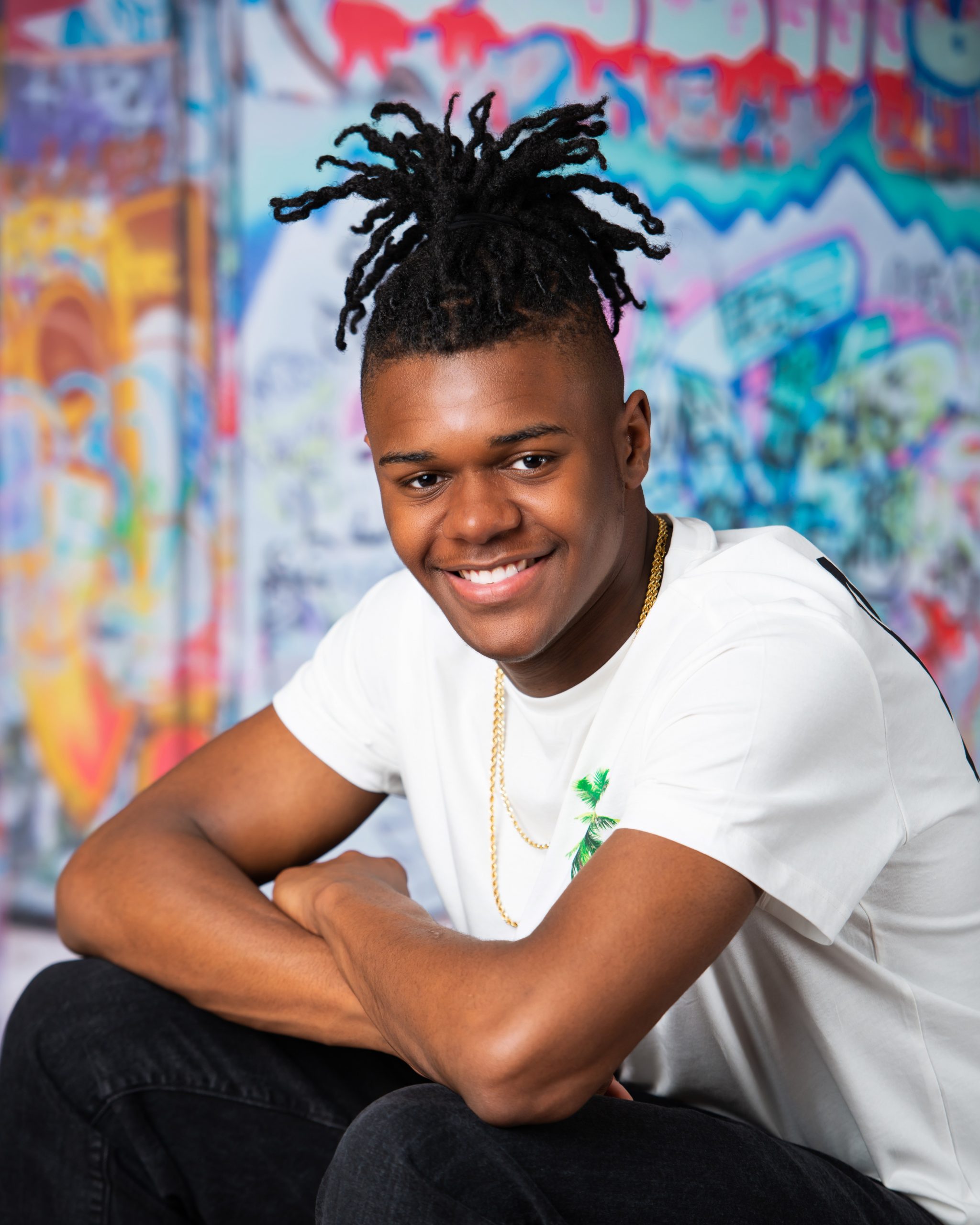 Frederick wearing graduation cap and sneakers on graffiti wall in studio session