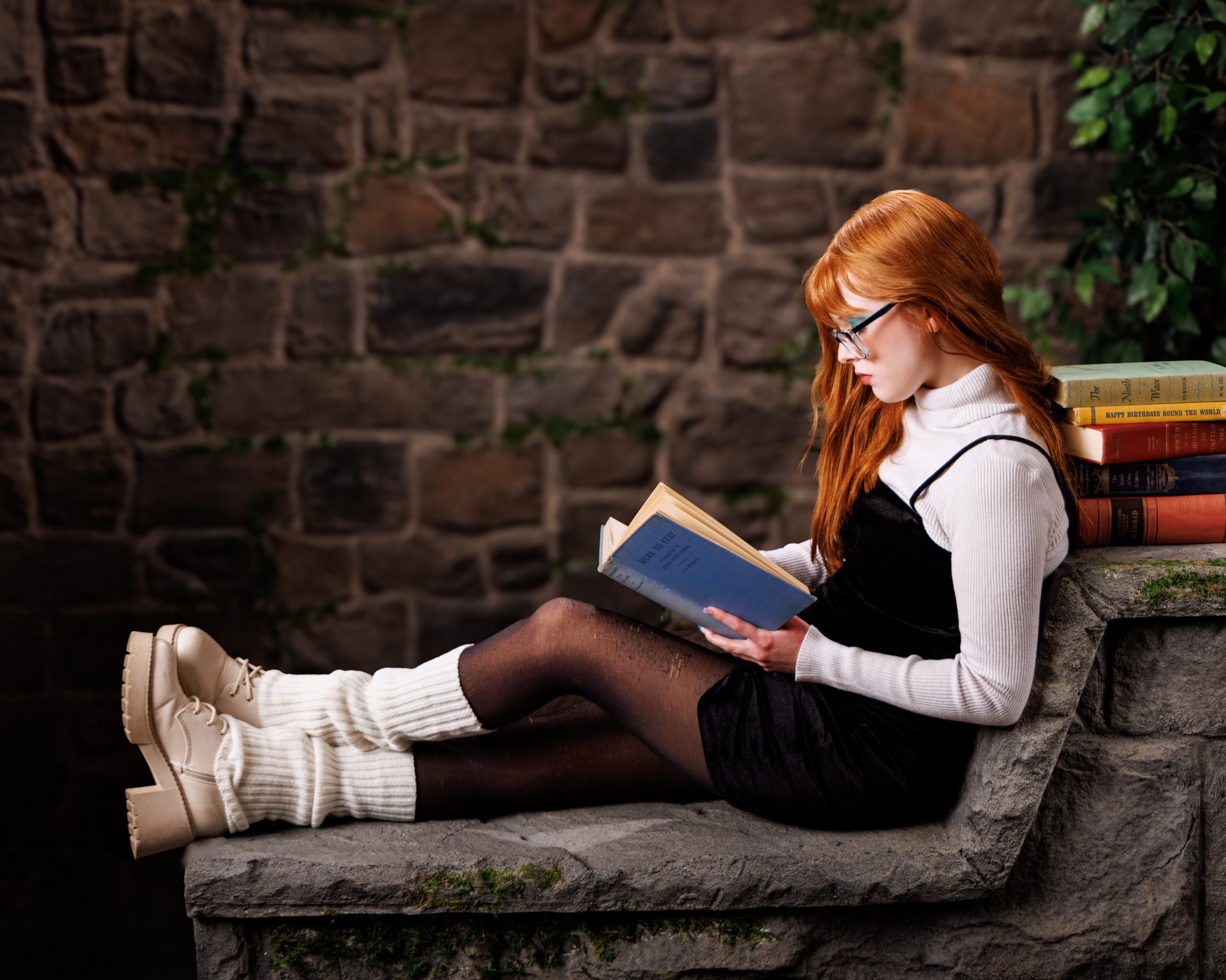 Senior model reading book on stone bench with stacked books in Downriver photography setting