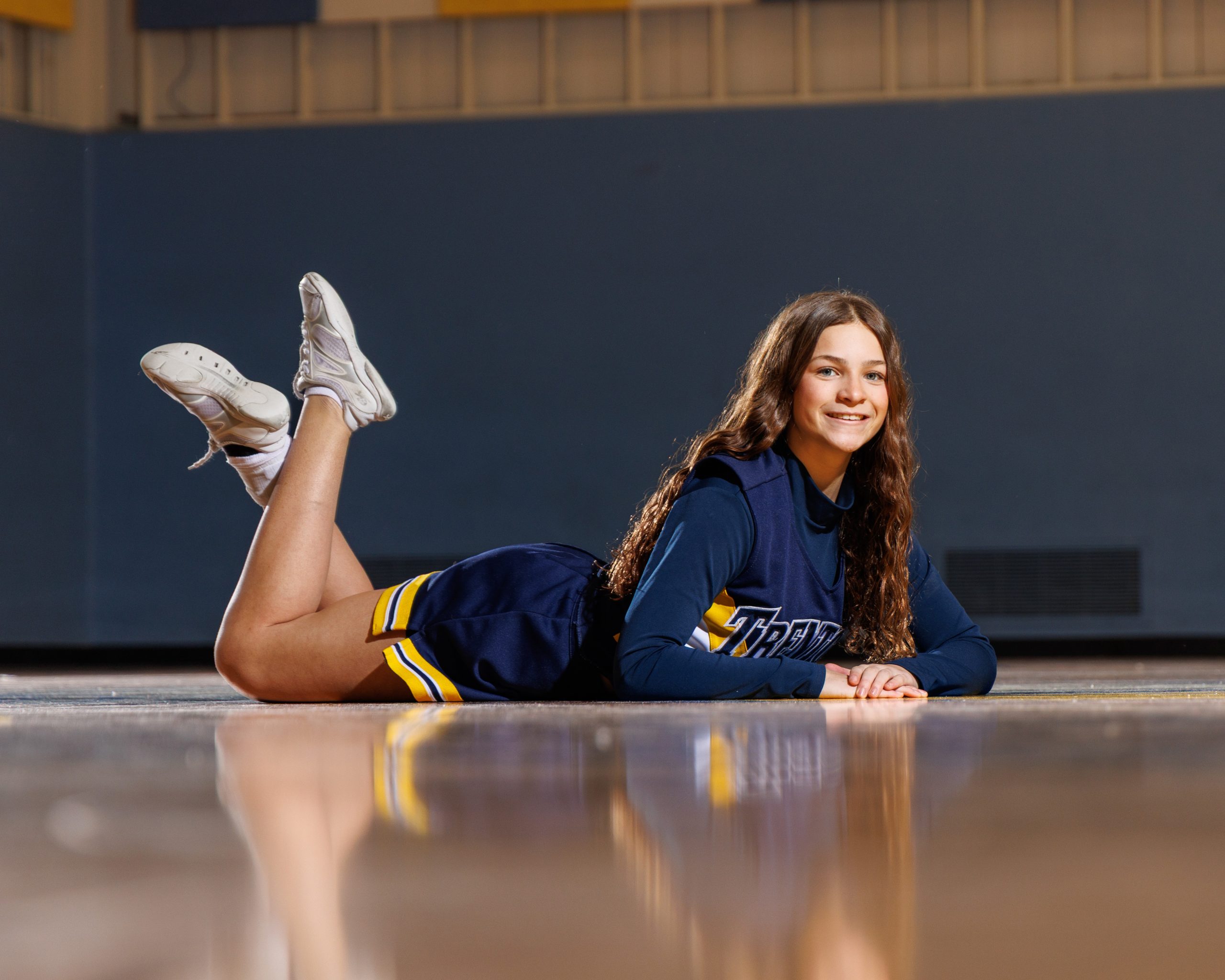 Cheerleader seated on gym floor in Trenton uniform during portraits session