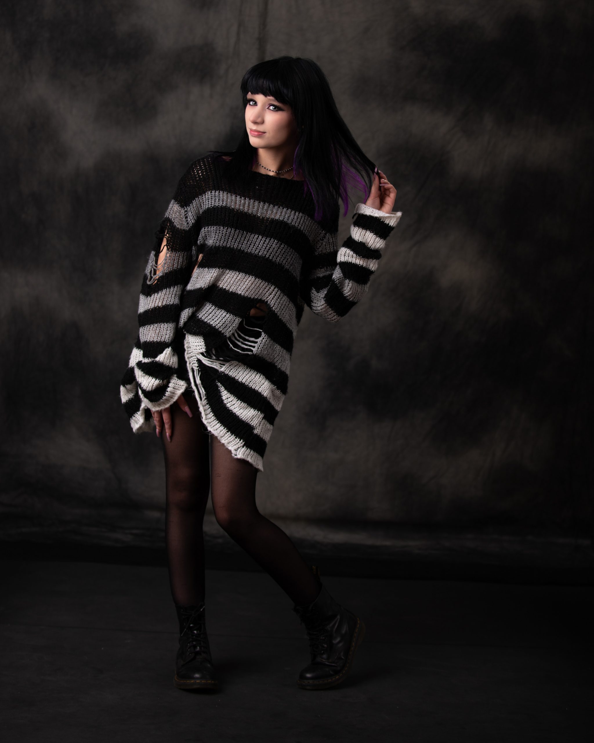 Gothic-themed senior portrait of Ashley wearing a black and white striped sweater with purple hair accents