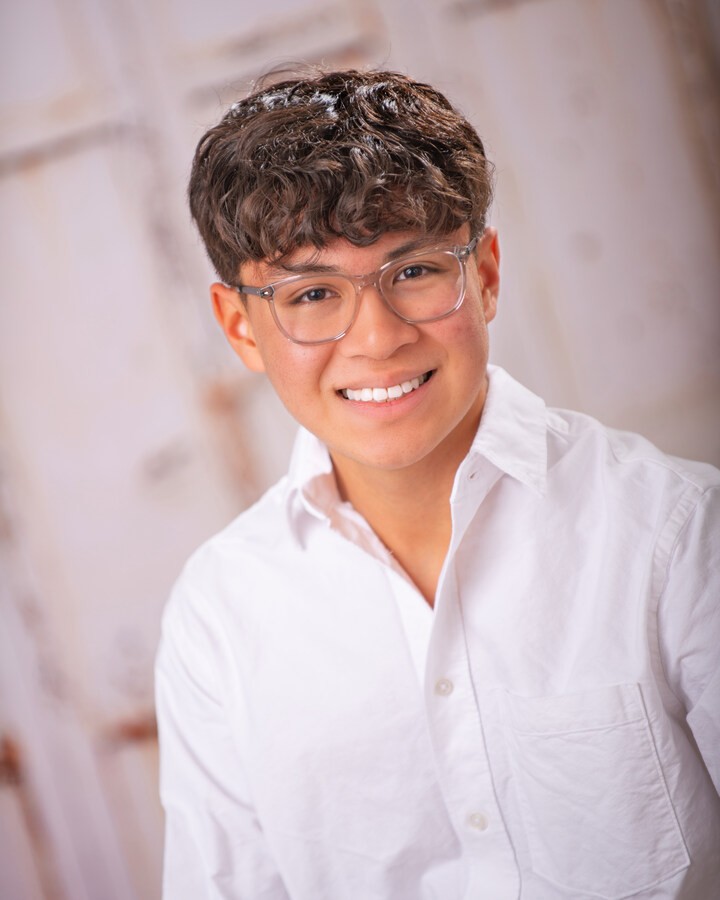 Professional headshot of a young man in a black suit with hands clasped, wearing glasses and a smartwatch, Downriver senior portrait session