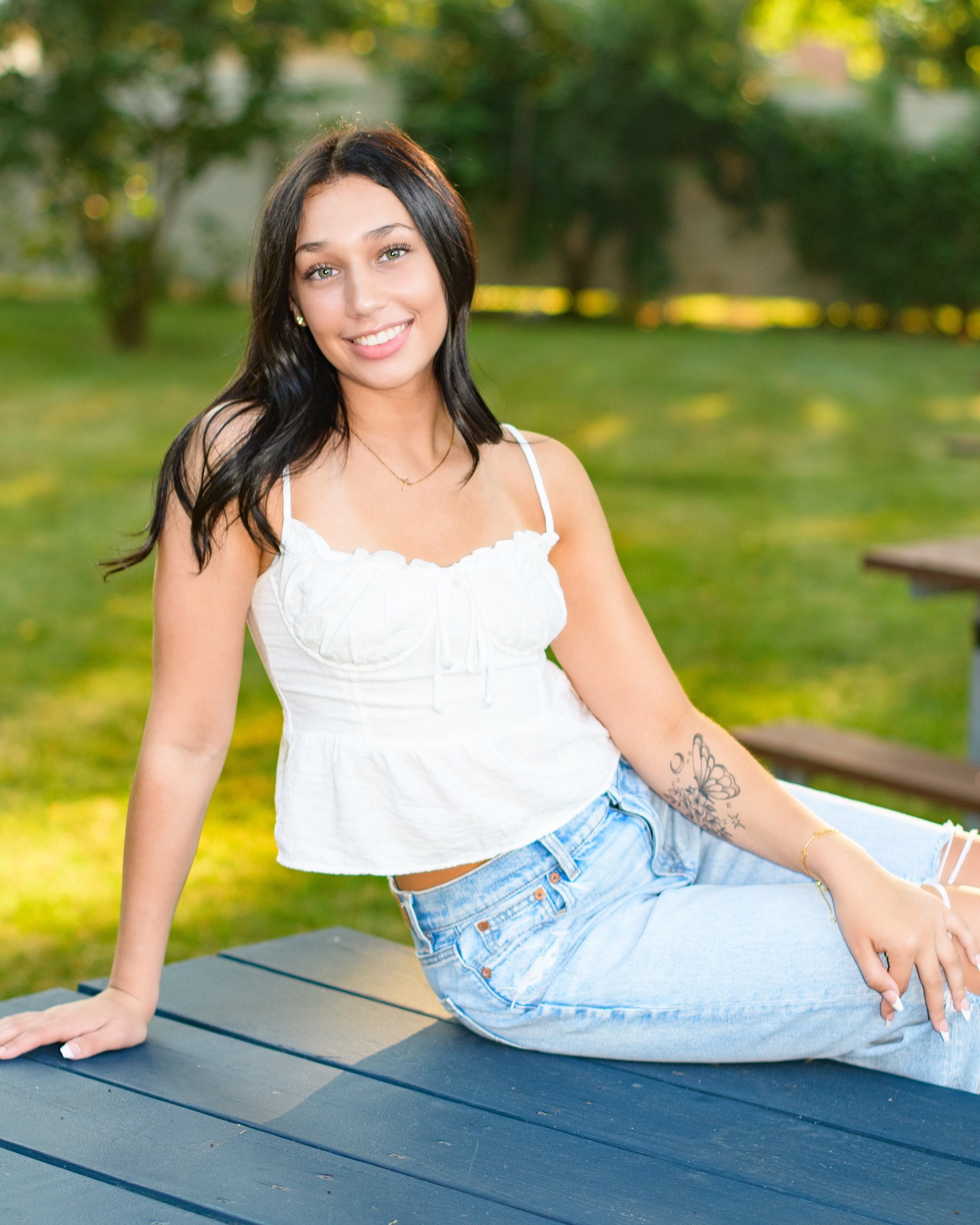 Natural light senior photography in a park setting, showcasing a young woman's casual style with a visible butterfly tattoo