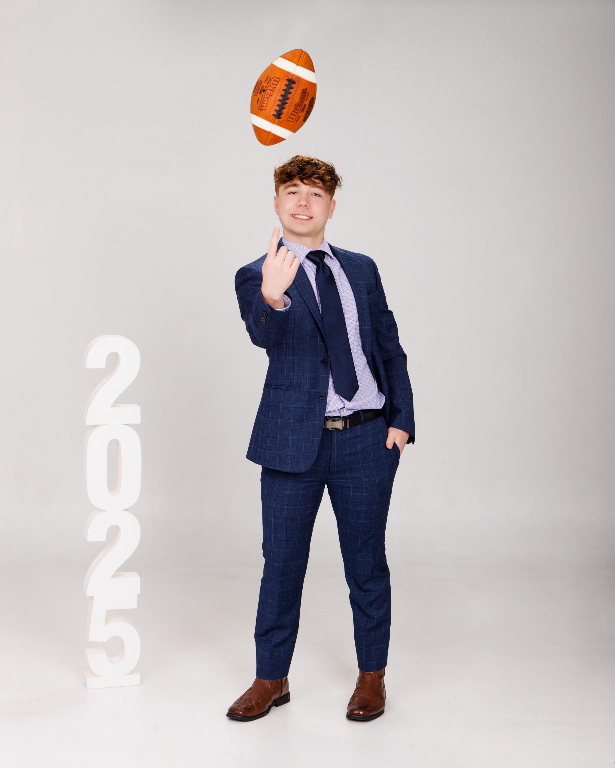 senior photo session with graduation gown, cap, and floating football prop