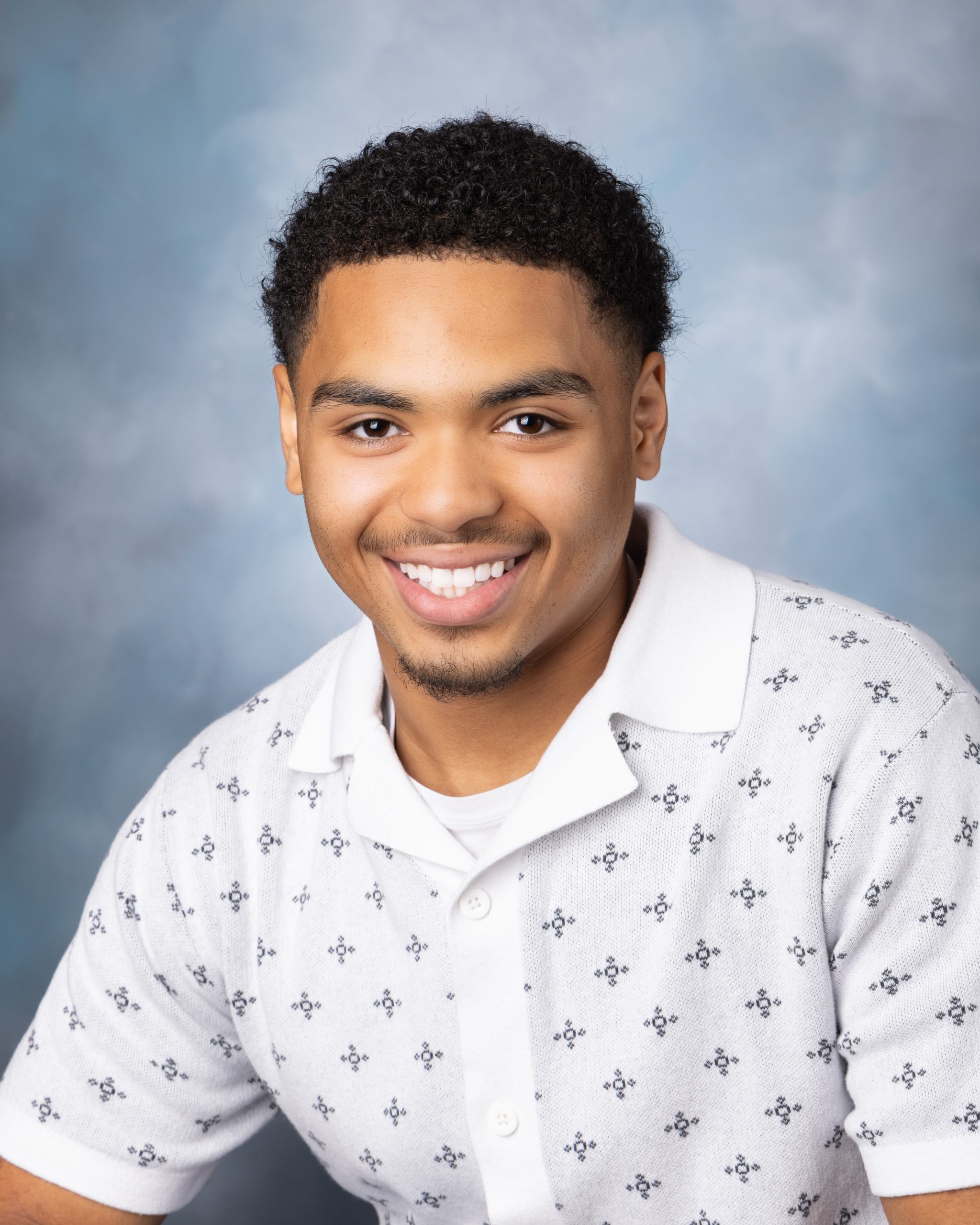 Professional senior yearbook portrait with short hair, light patterned polo shirt, and blue gradient studio backdrop