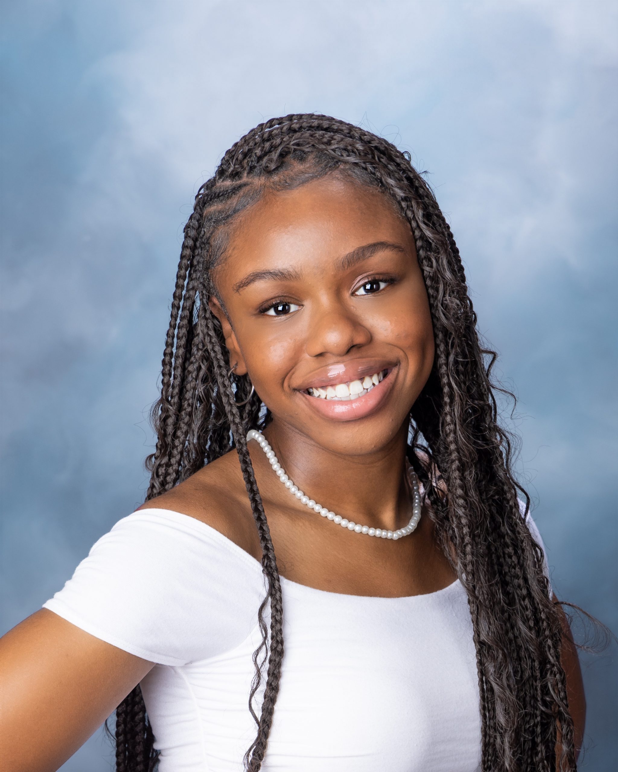 Senior headshot featuring braided hairstyle, black off-shoulder top, pearl necklace, and Downriver photography studio background