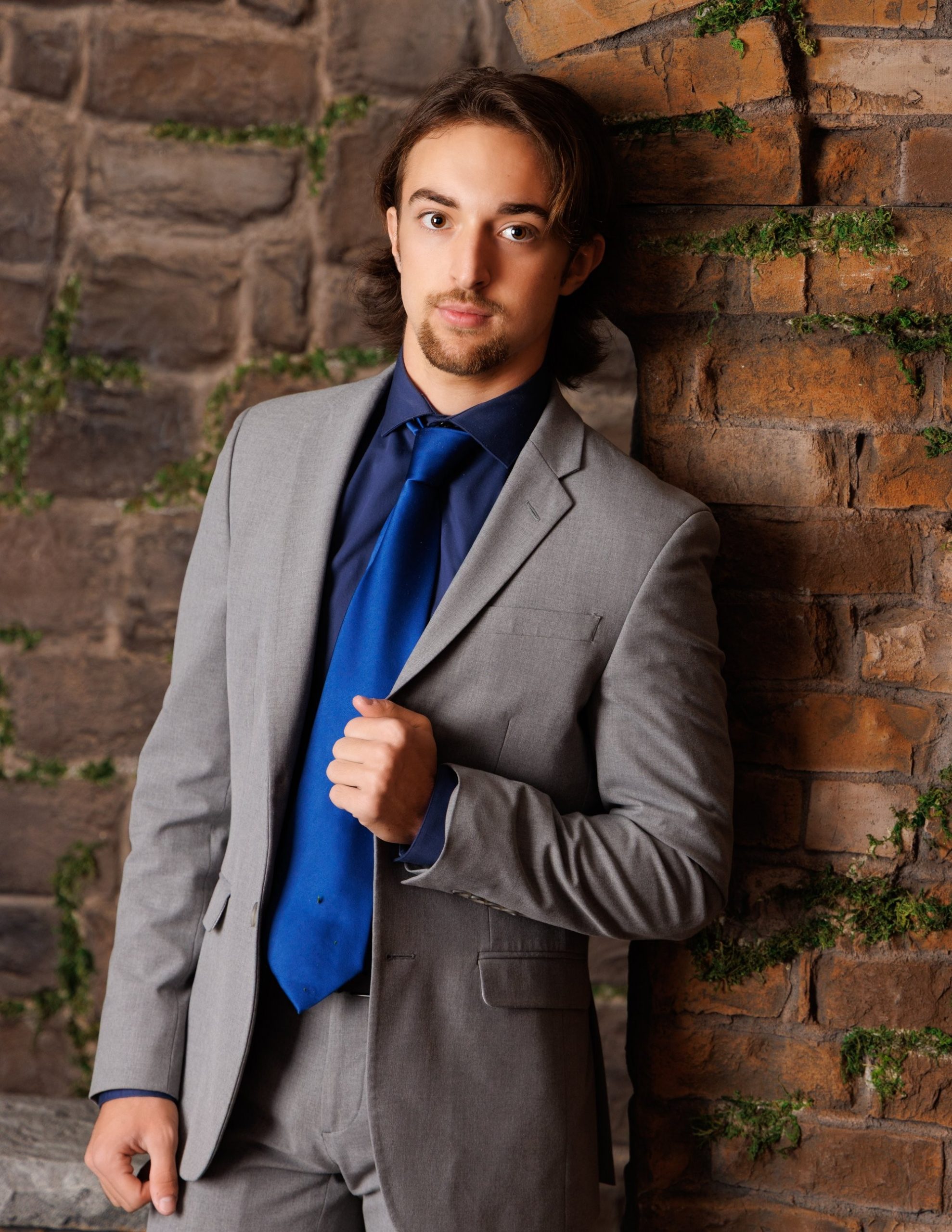 Formal portrait of Henry in a gray suit and blue tie leaning against a brick wall