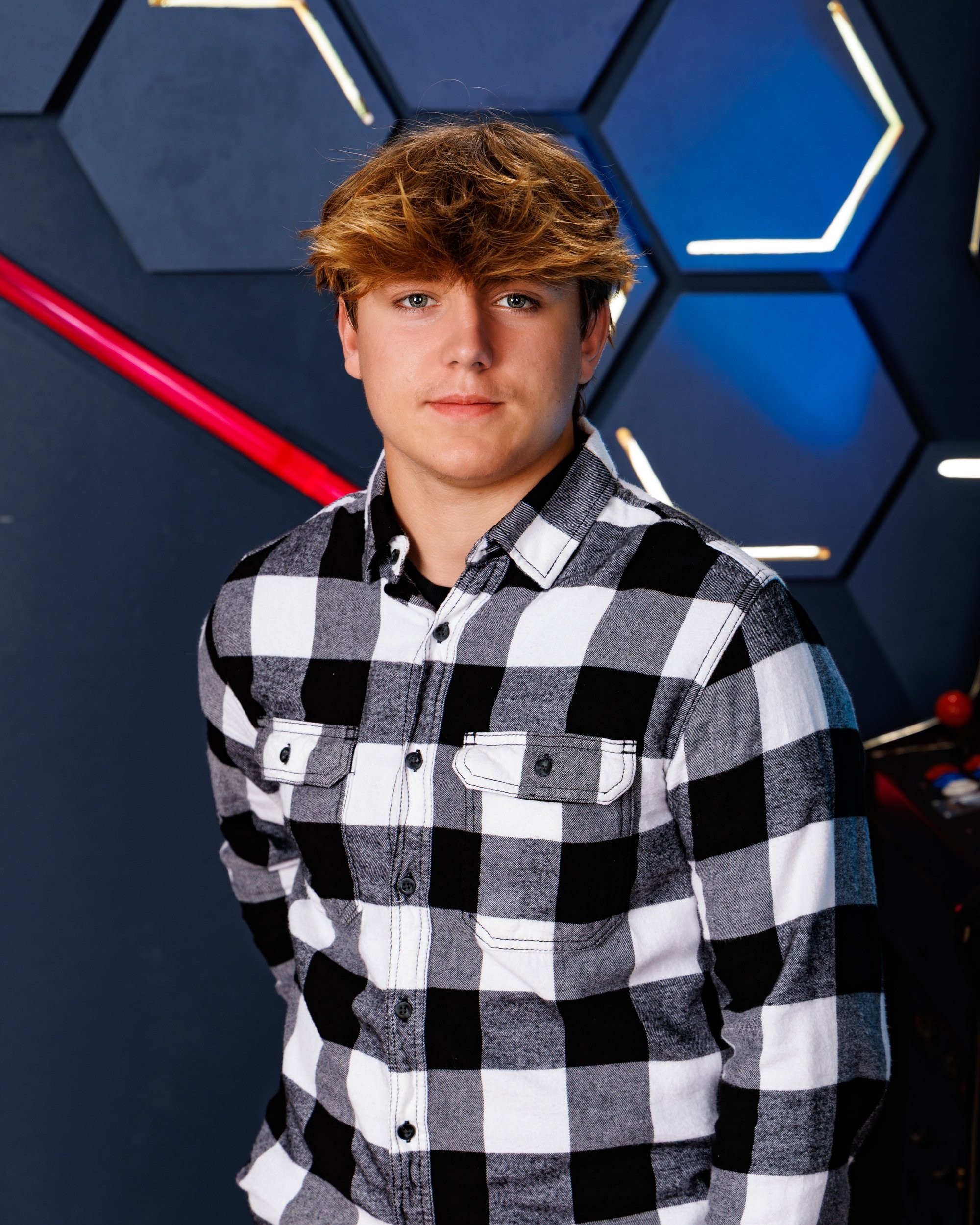 Ethan posing with a baseball bat near an arcade game in modern studio setting