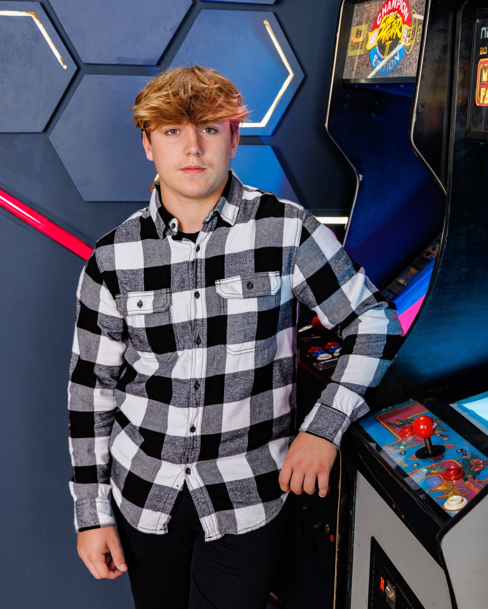 Ethan posing with a baseball bat near an arcade game in modern studio setting