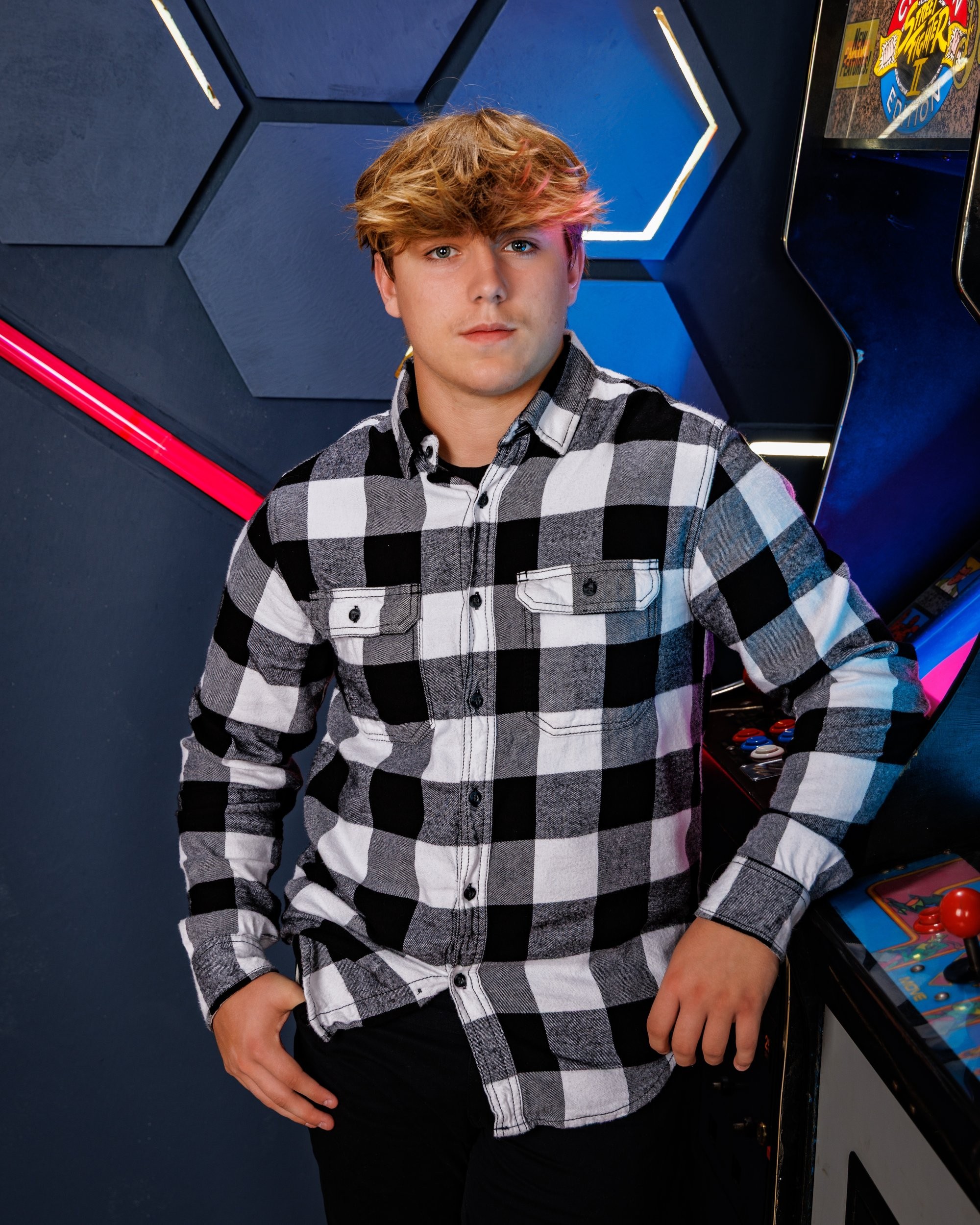 Ethan posing with a baseball bat near an arcade game in modern studio setting