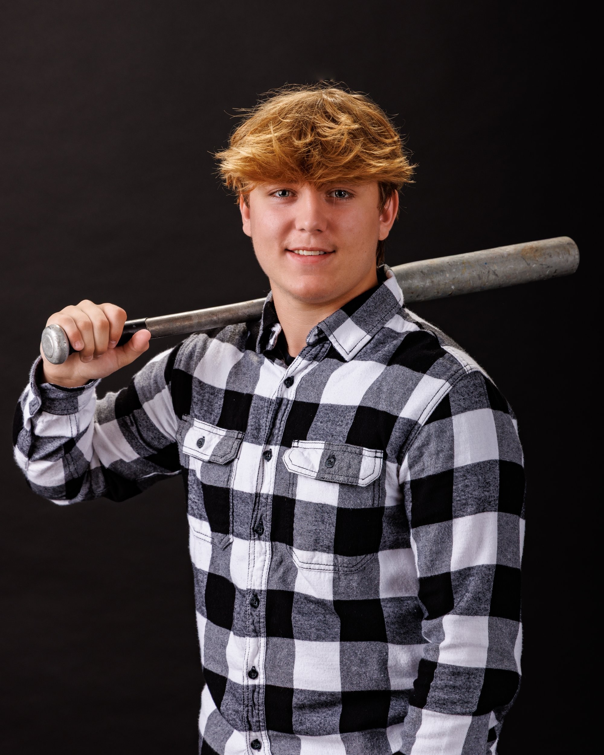 Ethan posing with a baseball bat near an arcade game in modern studio setting