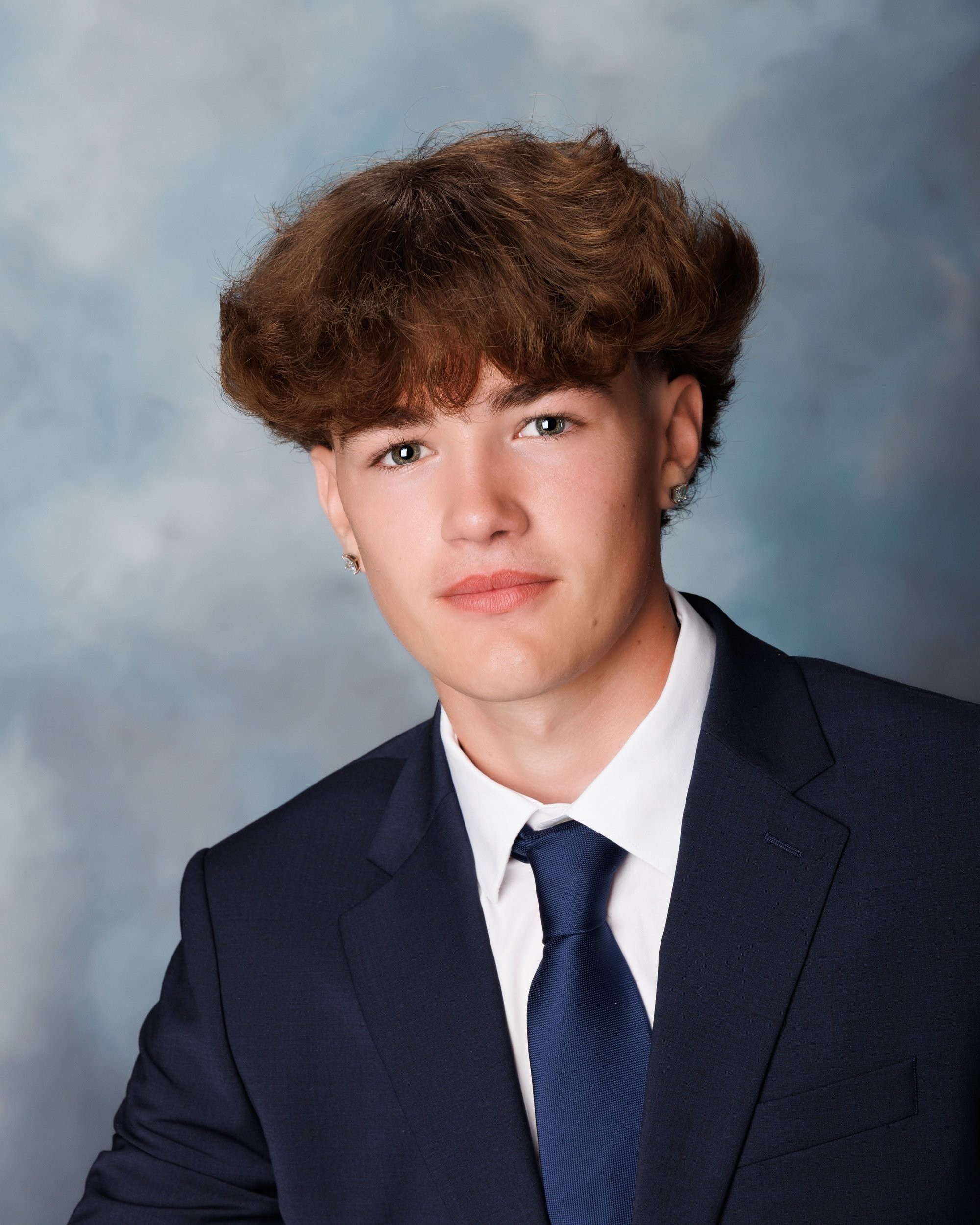 Evan holding an orange basketball in a navy suit and white shirt, posing for senior portraits with a light gray background