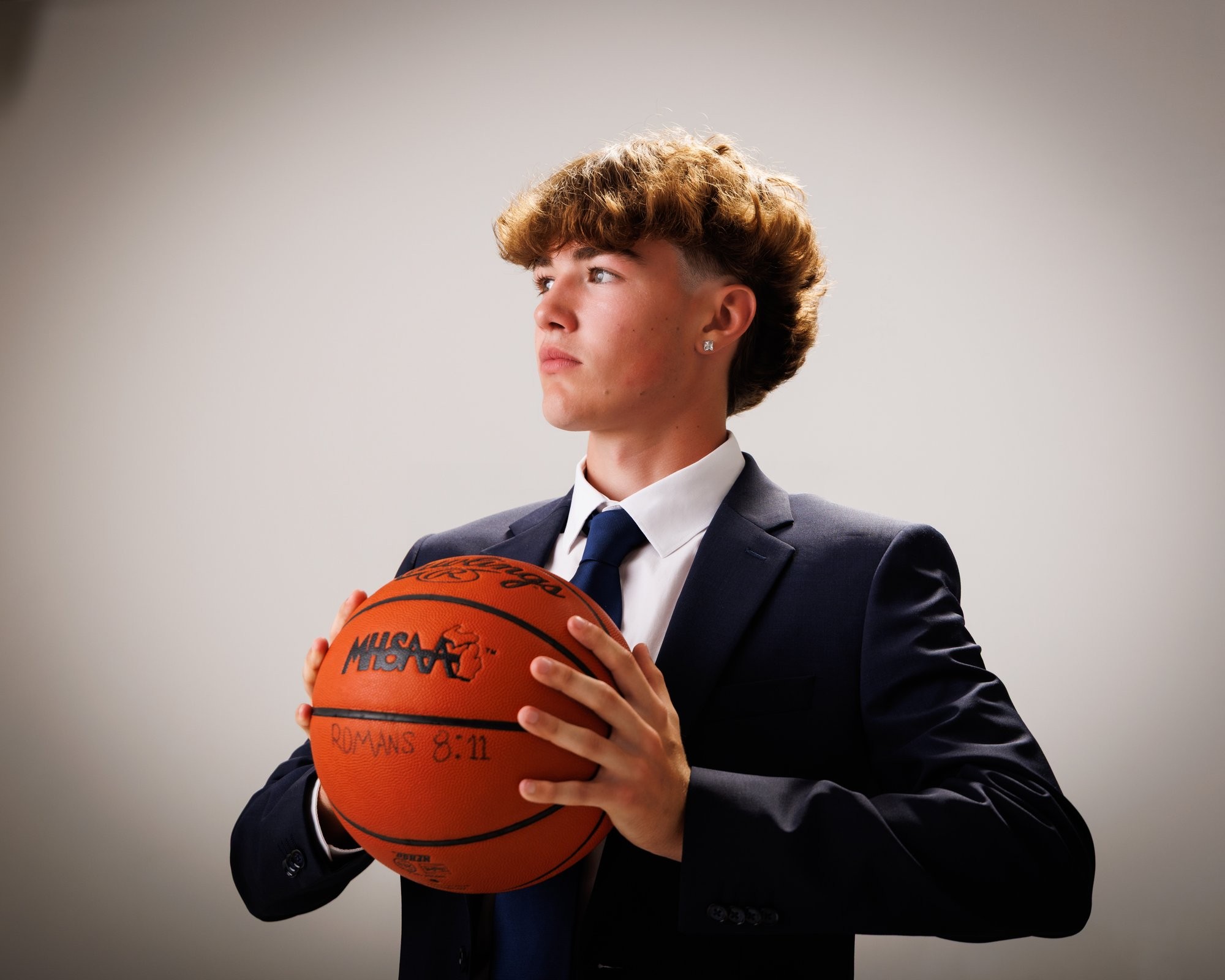 Evan in a navy suit and tie, smiling confidently against a dark studio backdrop for senior photos