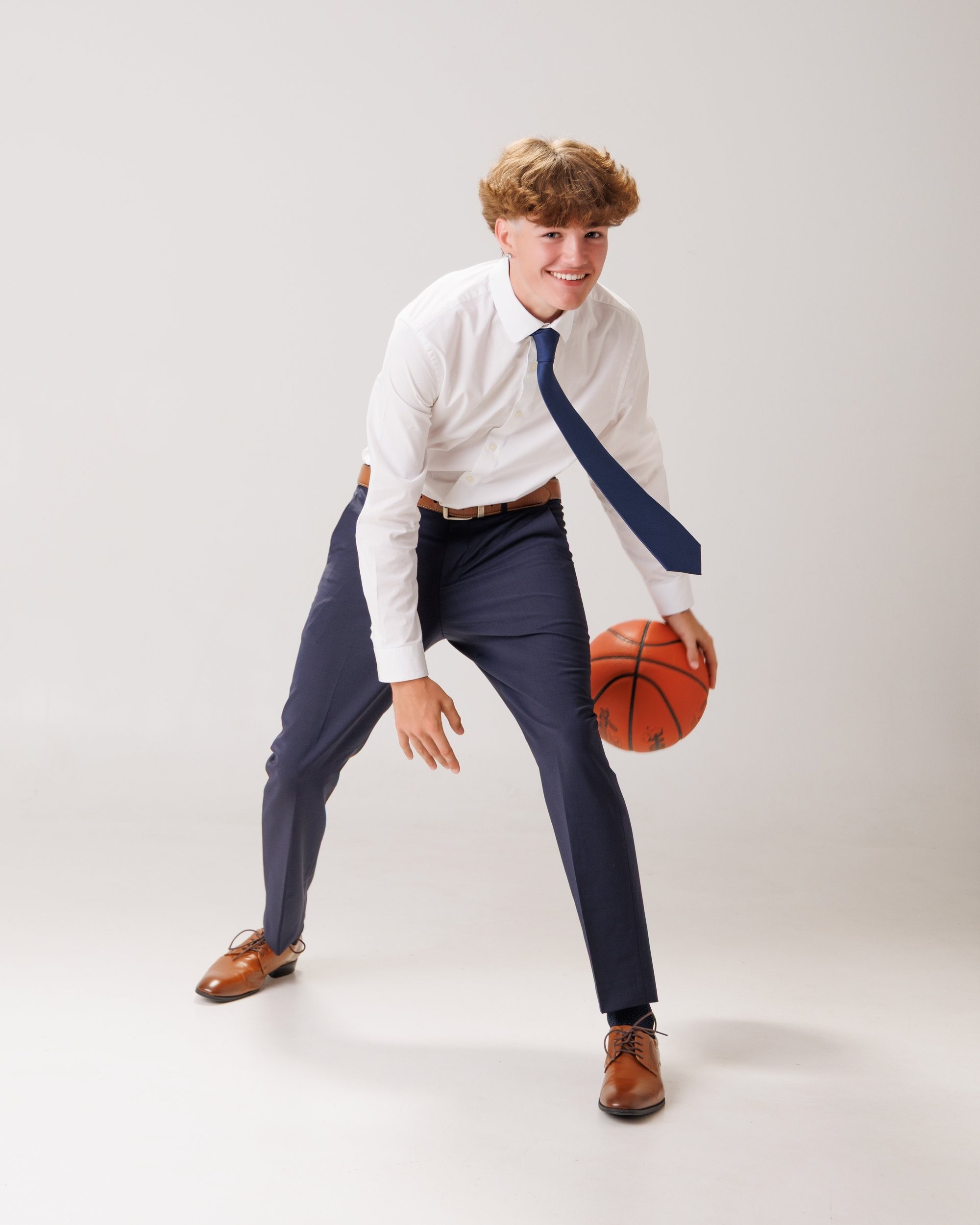 Evan in a navy suit and tie, smiling confidently against a dark studio backdrop for senior photos
